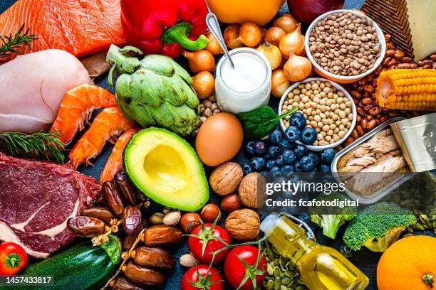 Various fresh vegetables, fruits, nuts, grains, and dairy products arranged on a table.
