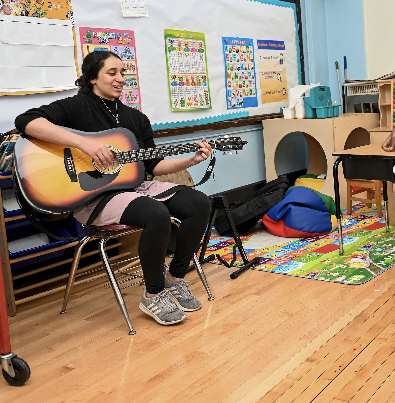 A music therapist is playing guitar in an elementary school classroom.