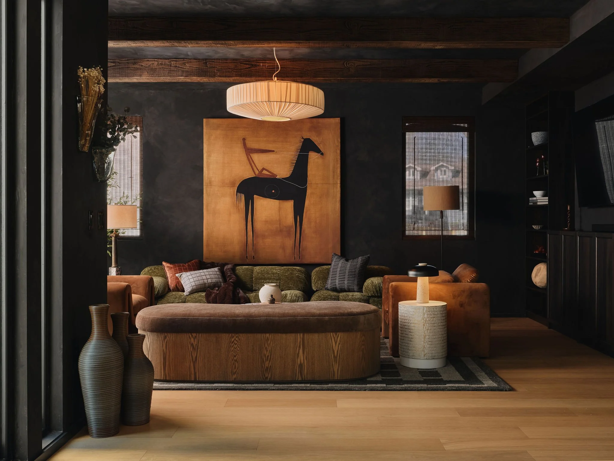 Living room with green sofa, orange armchairs, and wood accents, featuring a large horse painting and modern lighting.