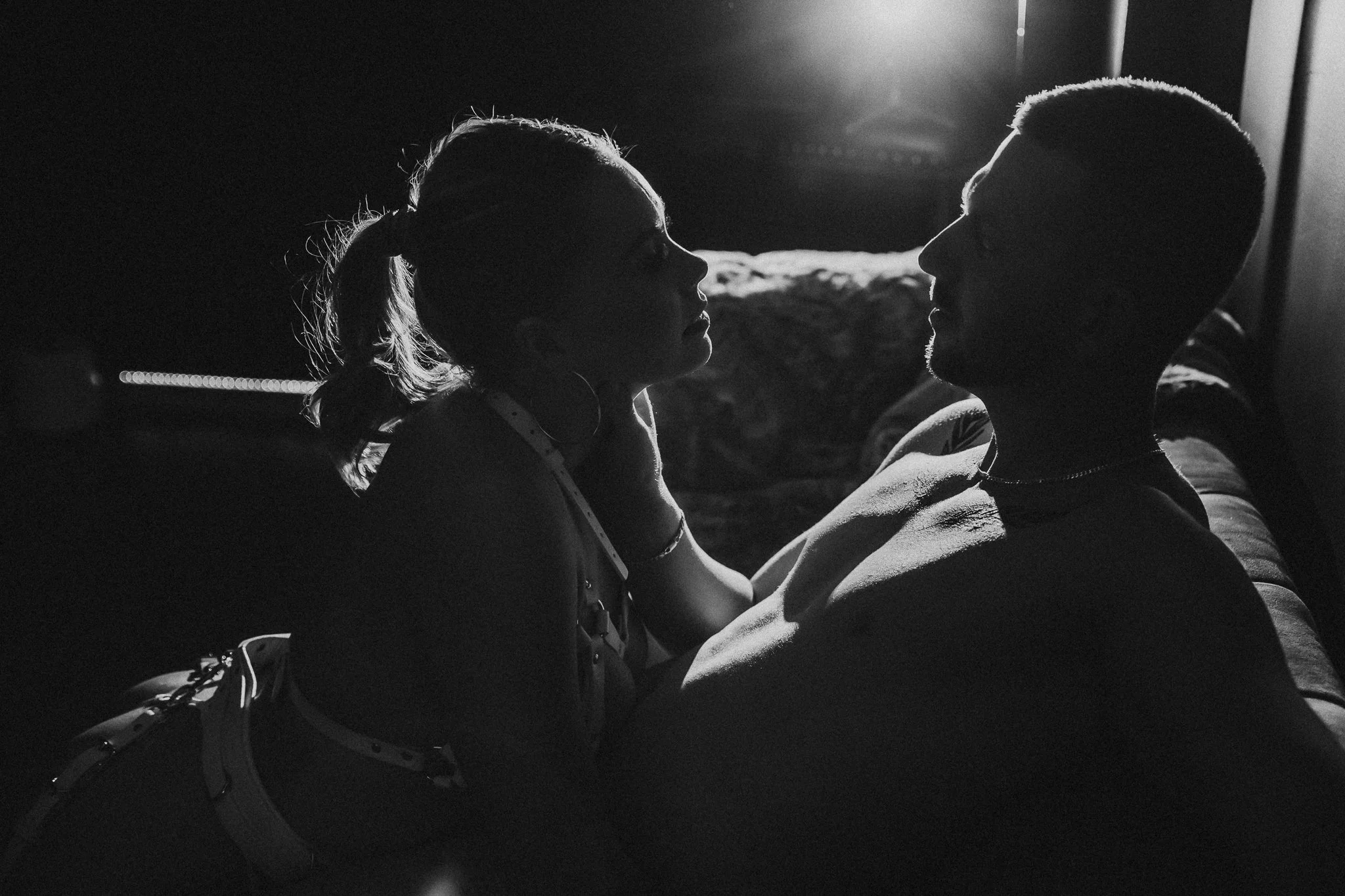 Silhouetted image of a woman and man sitting close together indoors, staring at each other, backlit by a bright light source.