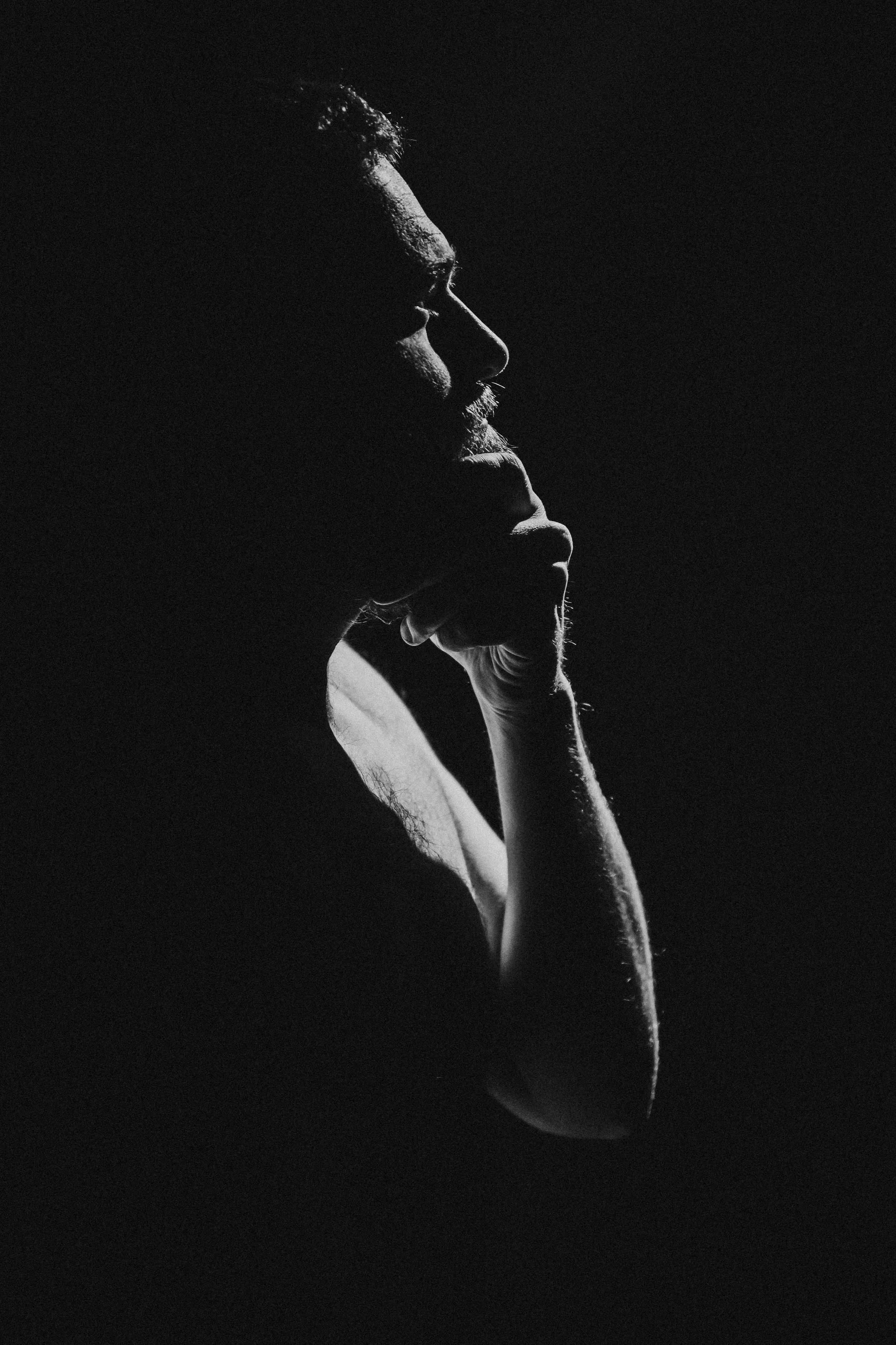 Black and white silhouette of a man resting his chin on his hand, with side profile and thoughtful expression, illuminated by soft light.