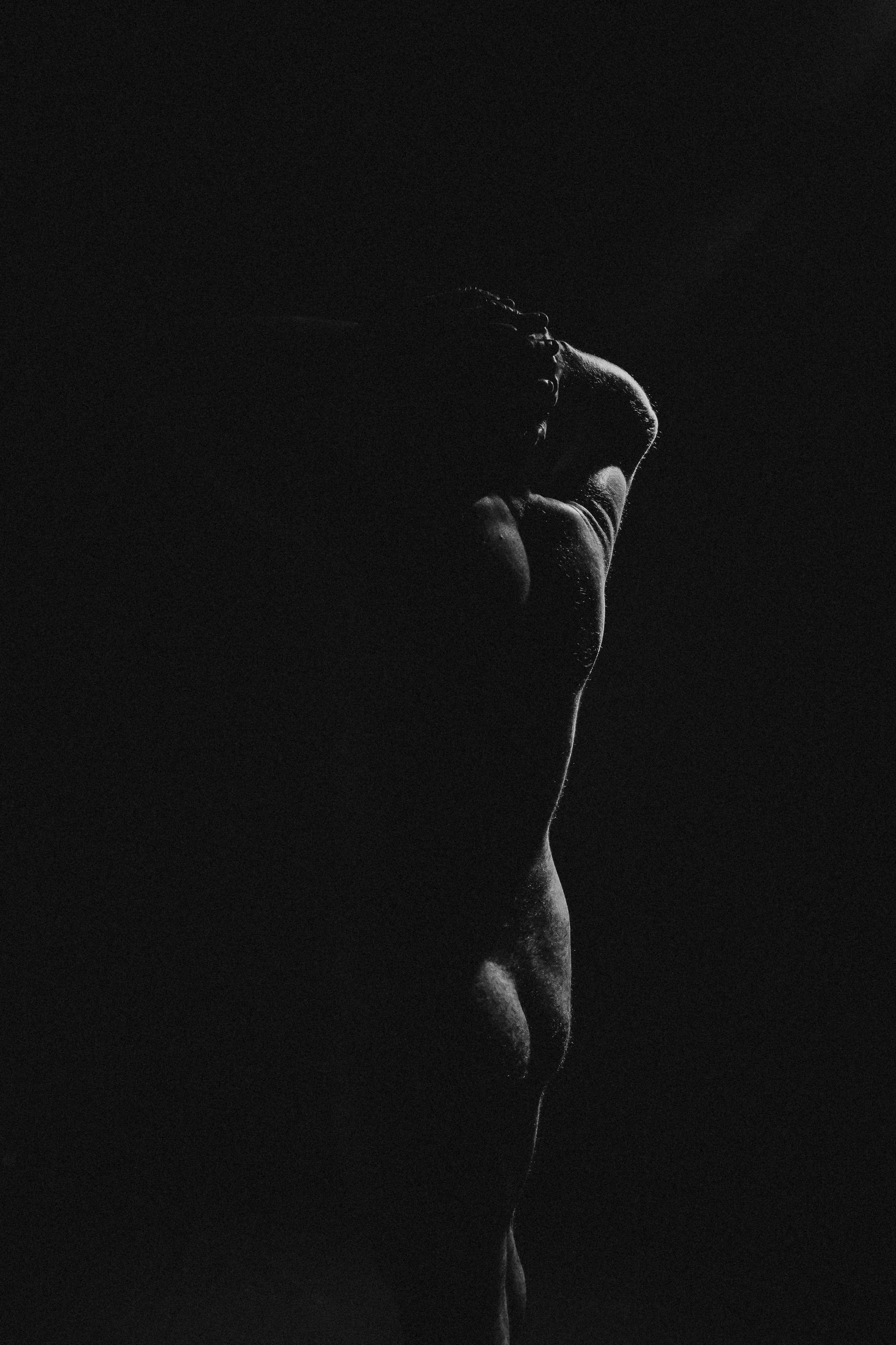 Close-up of a person's face and neck in profile, partially illuminated against a dark background.