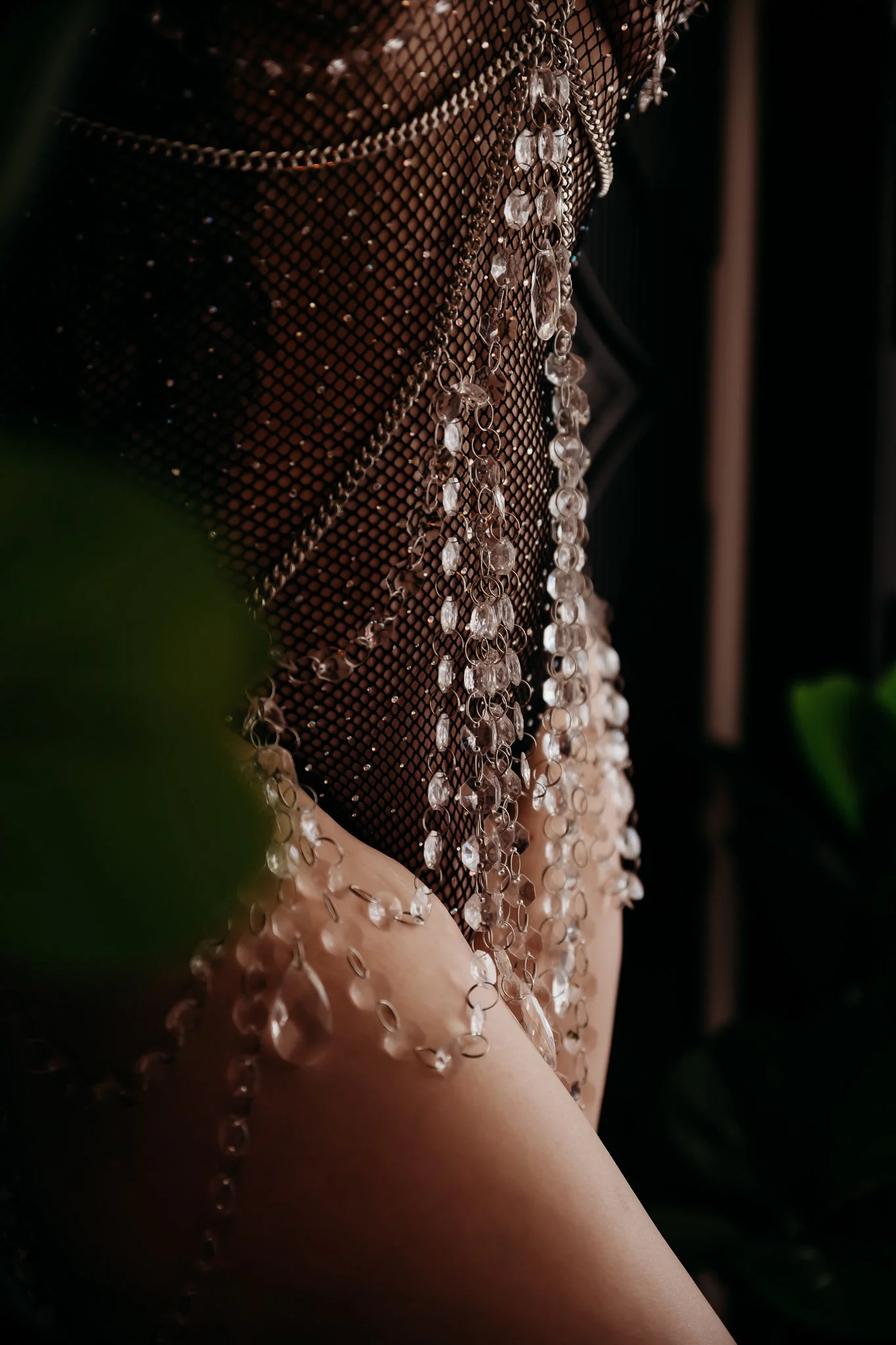 Close-up of a person wearing a black fishnet top adorned with long, dangling rhinestone chains, with bare skin visible through the fishnet.