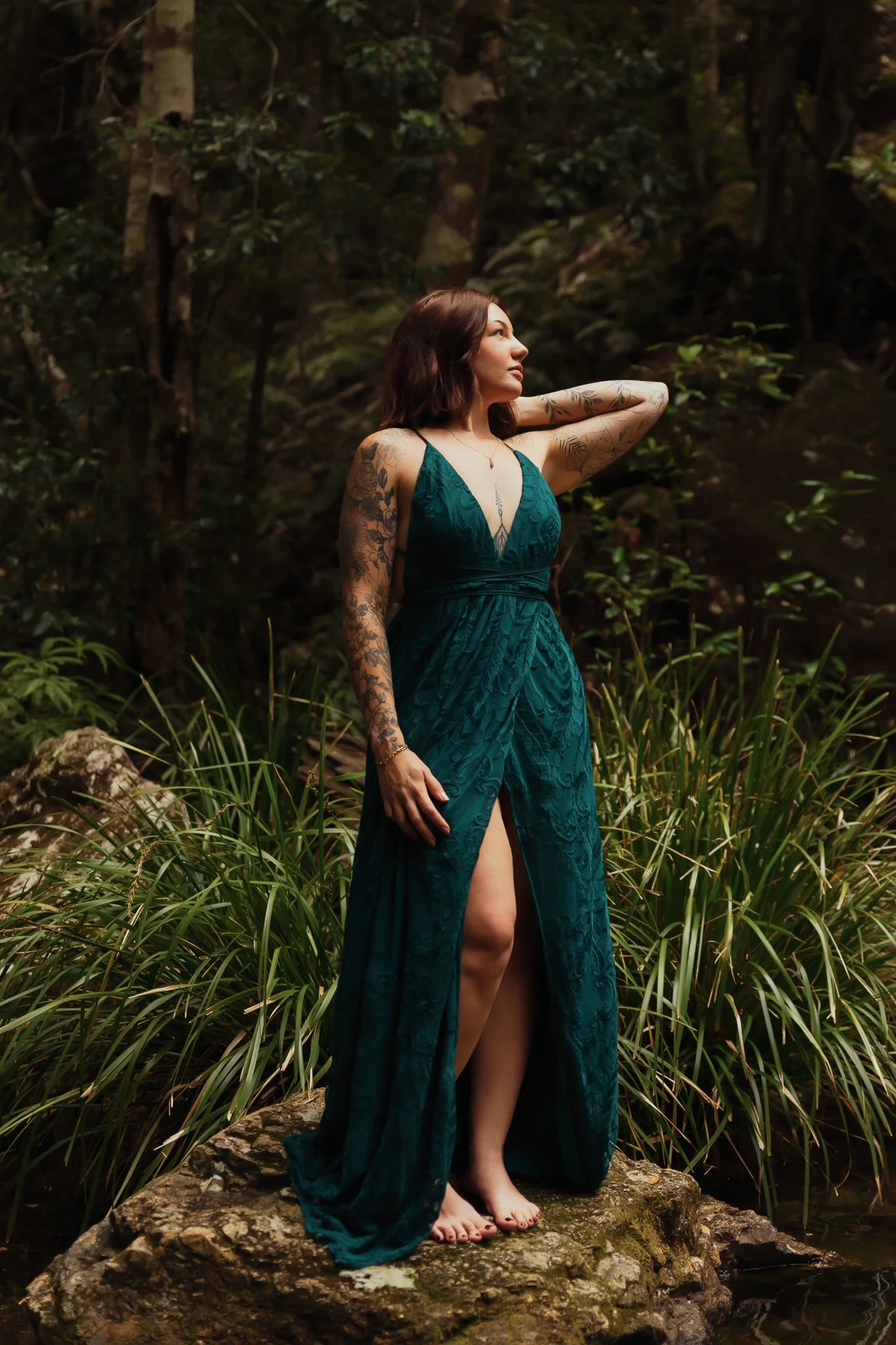 A woman in a teal dress standing on a rock in a forested area