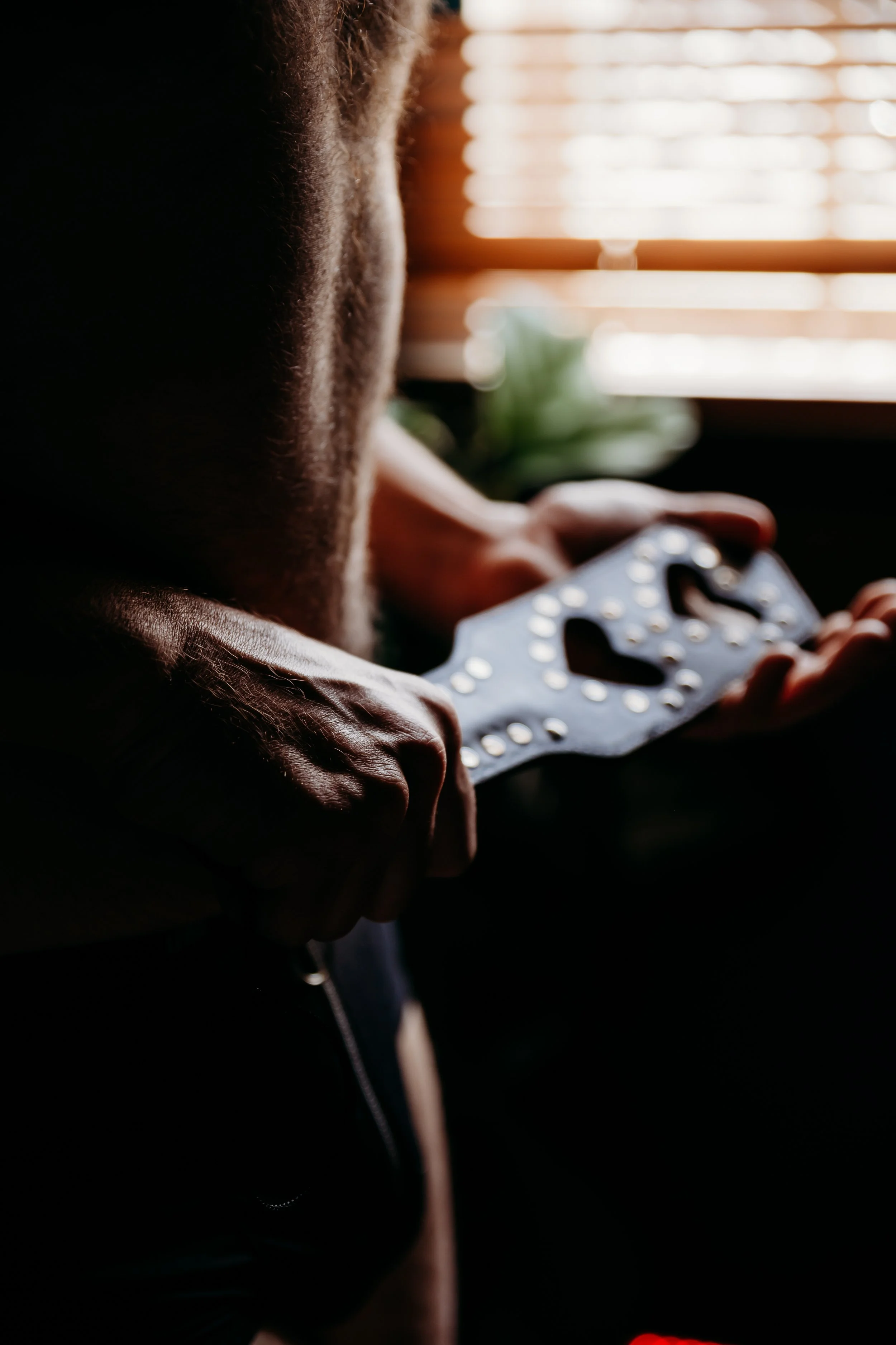Person holding a decorated mask with heart shapes and dots, indoors near a window with blinds.