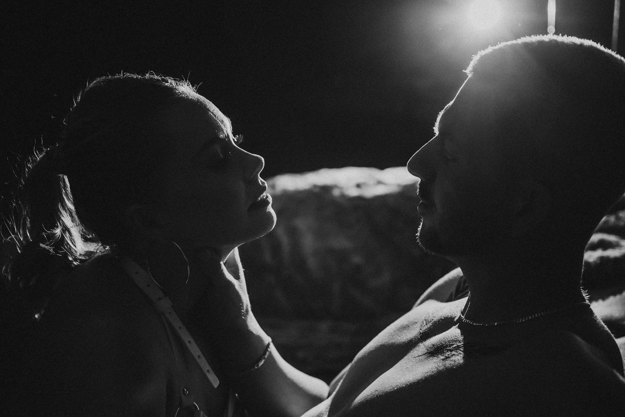 A black and white silhouette of a couple facing each other, with the sun illuminating their profiles from behind.