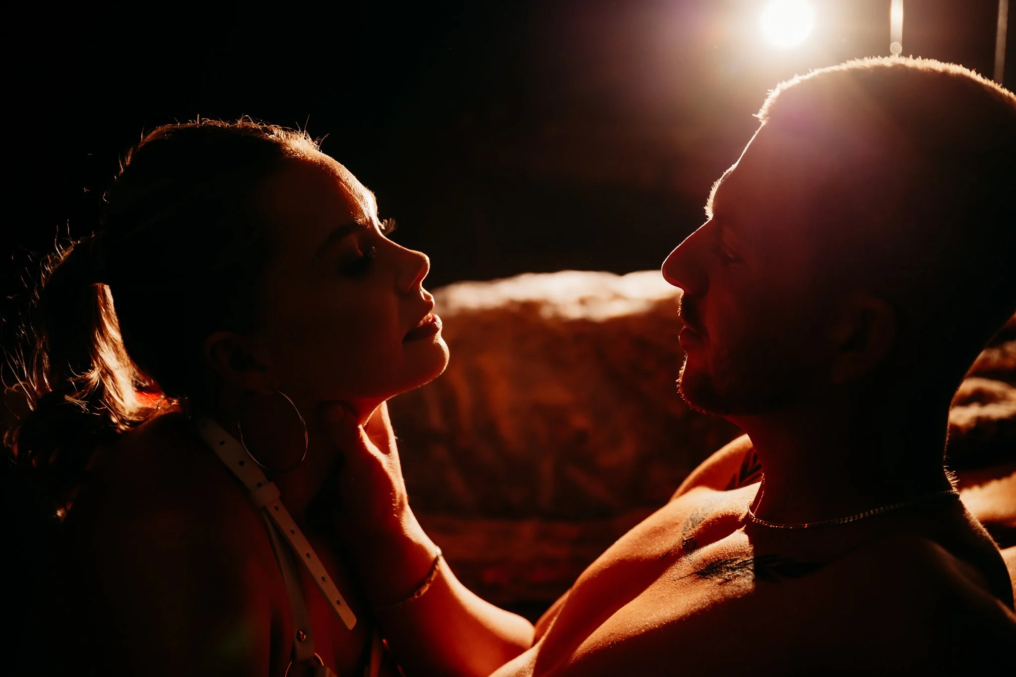 Silhouetted couple facing each other in intimate moment with backlighting, dark background.