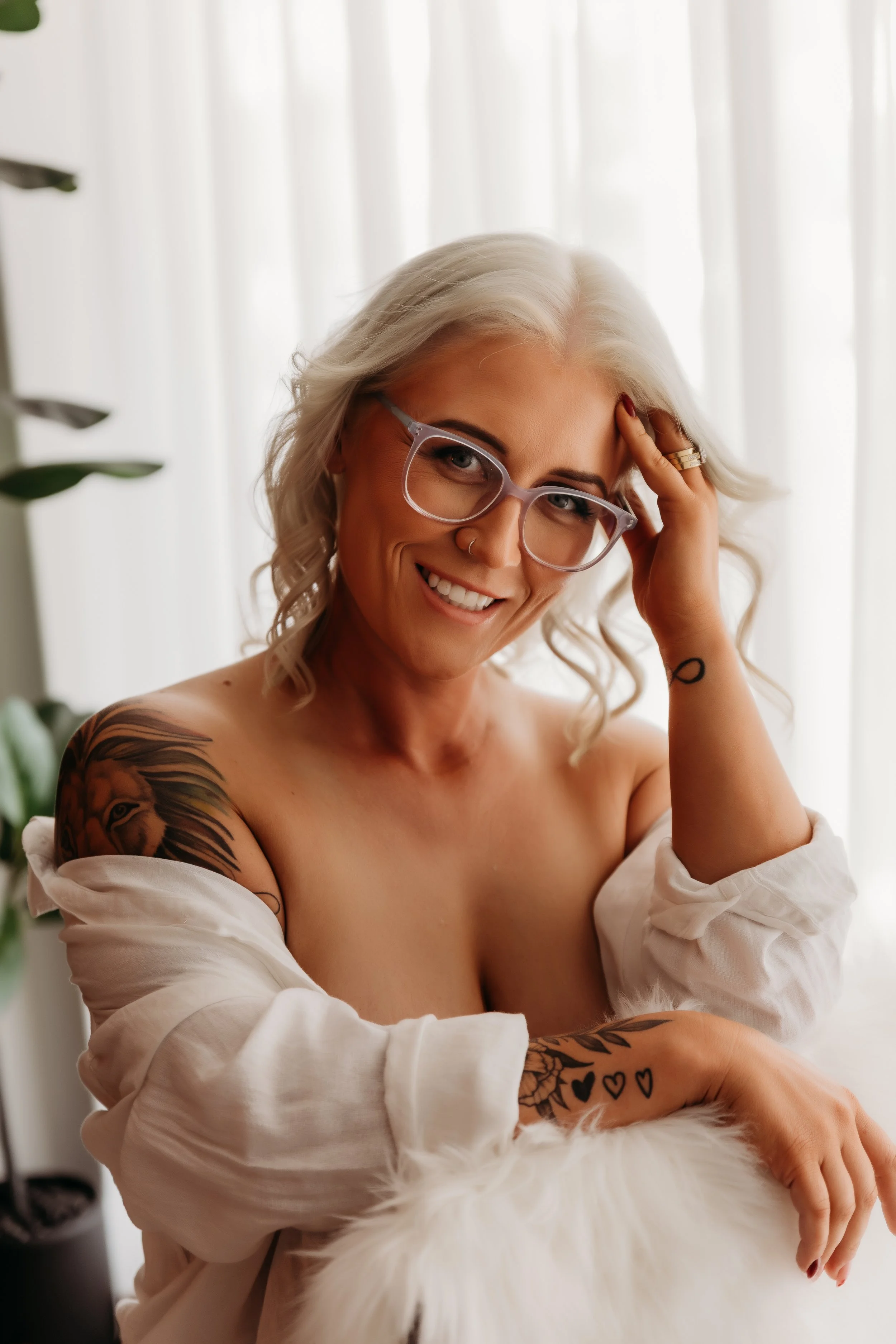 A woman with blonde hair, glasses, and tattoos smiling while petting a white and orange cat.