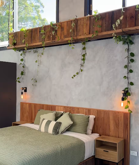 Bedroom with wooden headboard, green bedding, pillows, and hanging green plants above the bed.