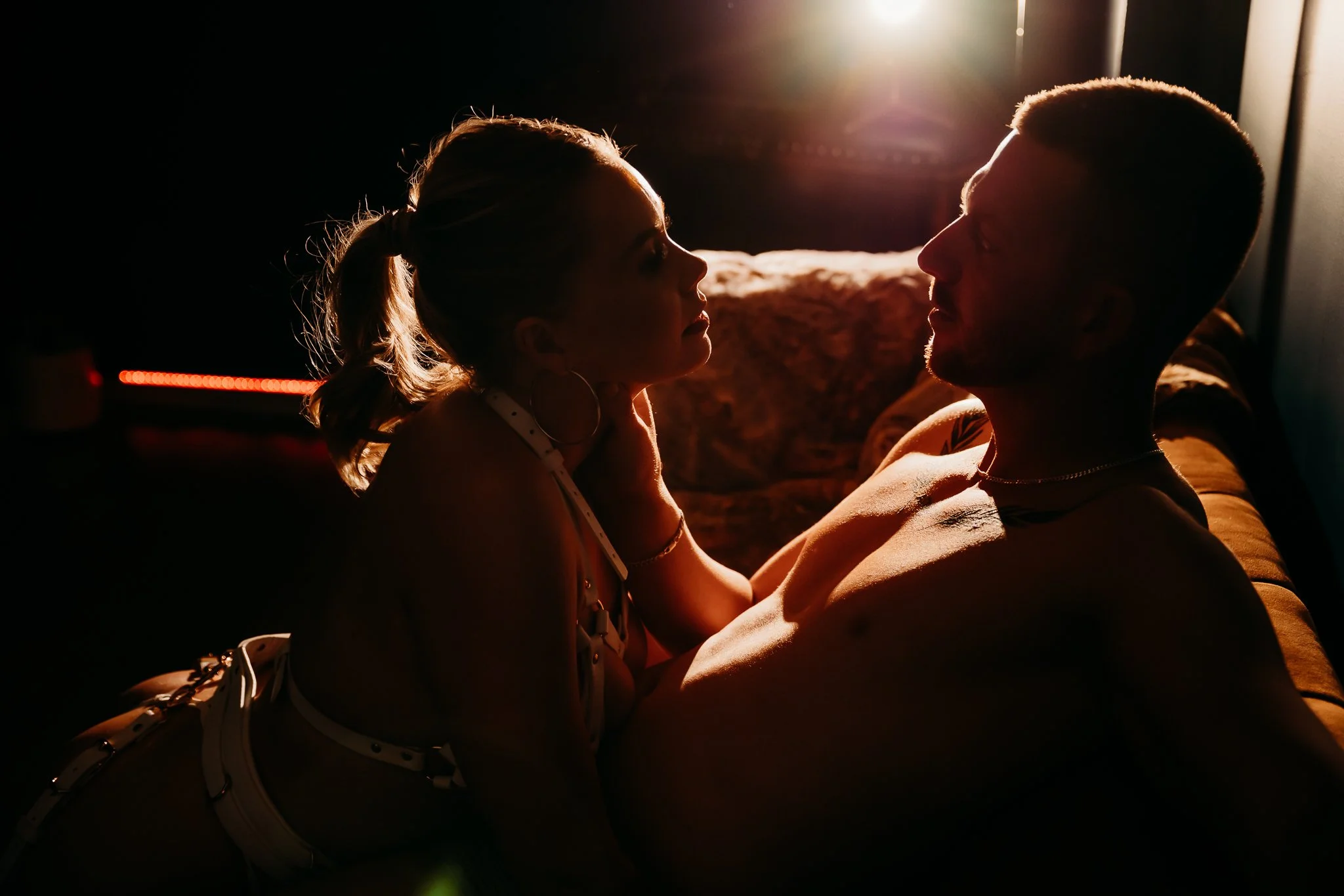 A man and woman in a close, intimate moment with backlit lighting creating silhouettes of their faces and bodies.