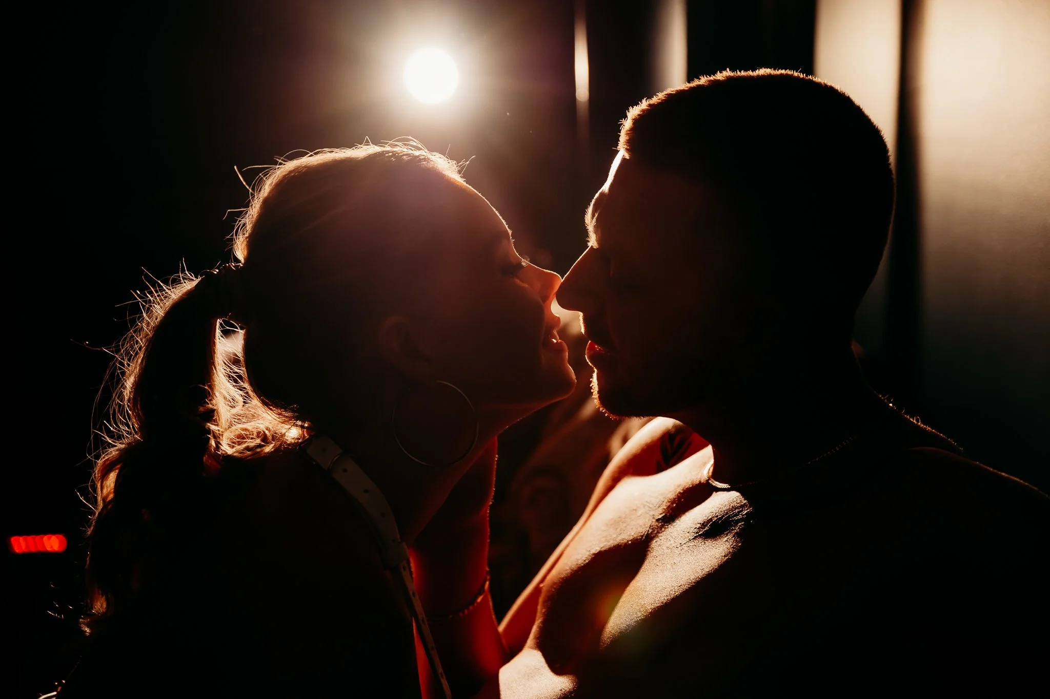 A silhouette of a woman and man close to each other, with a bright backlight creating a warm glow around their faces.