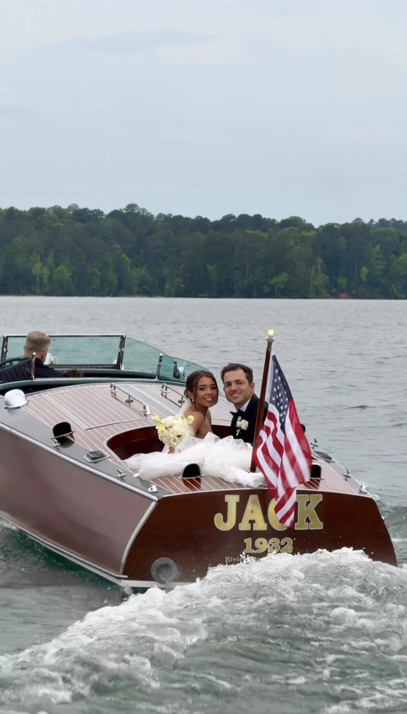 A bride and groom sitting on a boat celebrating their wedding, with the bride holding a bouquet and an American flag displayed.