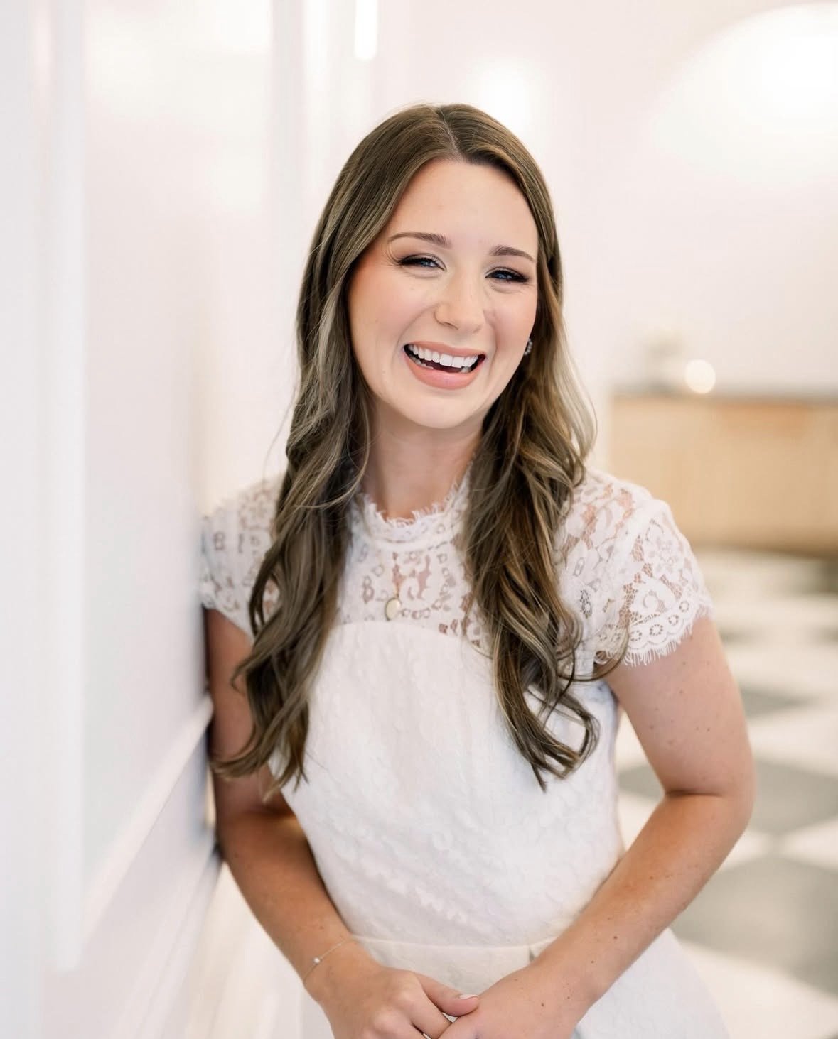 Two women standing together at a decorated event venue, smiling for the photo. The venue has a high vaulted ceiling with a chandelier and the tables are set with flowers, candles, and place settings.