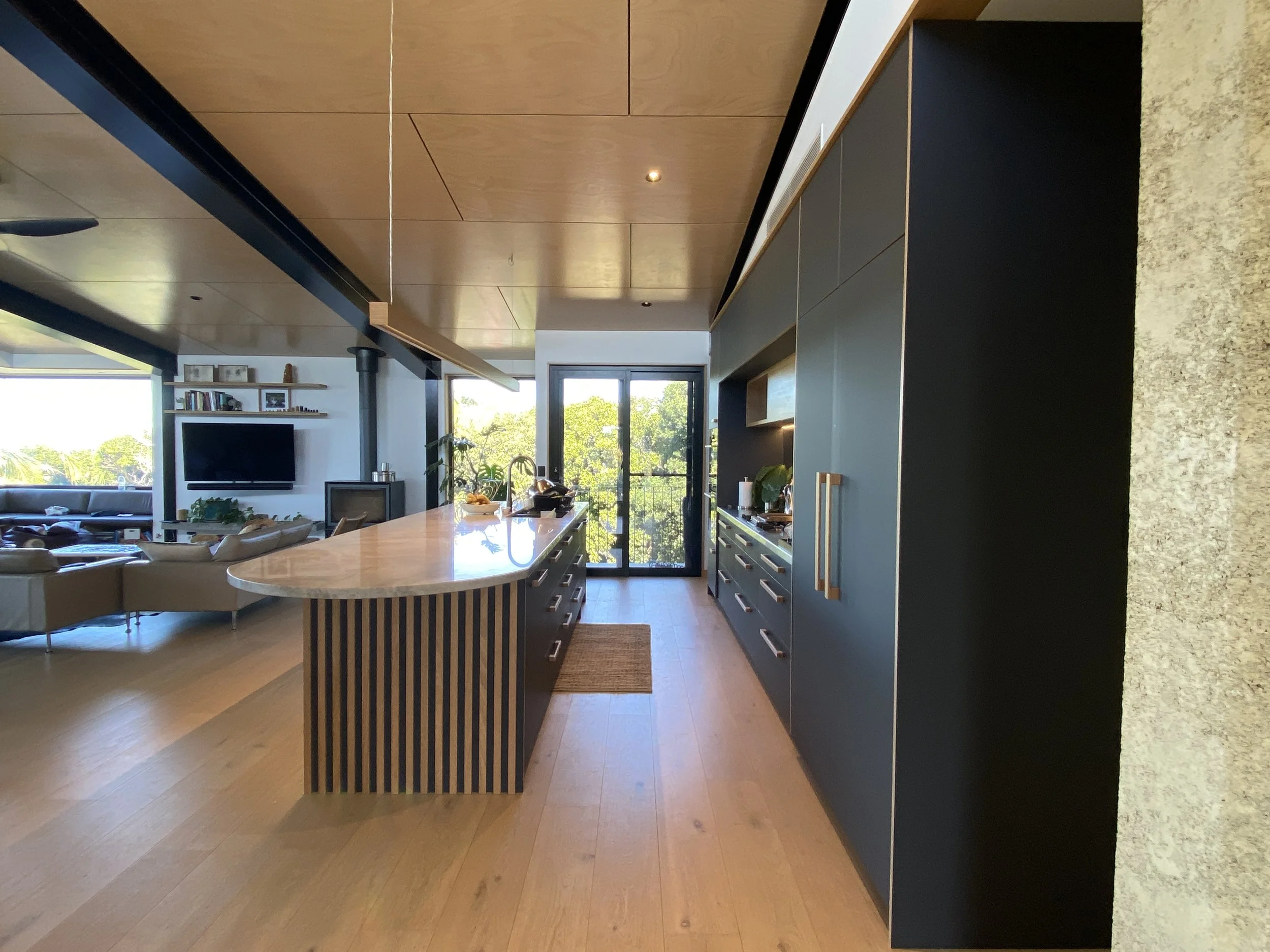 Modern kitchen with black cabinets, a marble-topped island, and large glass doors leading to a balcony with trees outside.