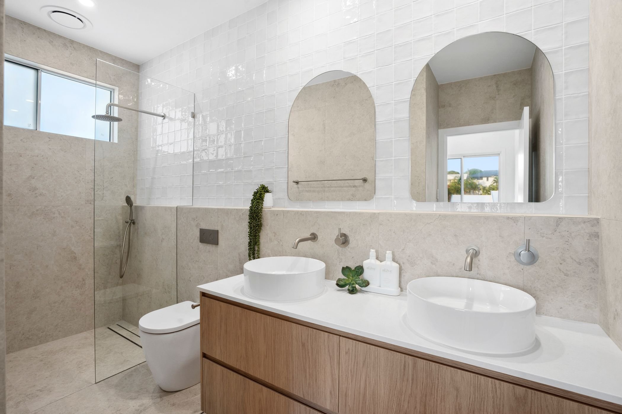 Boutique duplex project in Port Macquarie features modern bathroom with double vanity, arched mirrors, and walk-in shower.