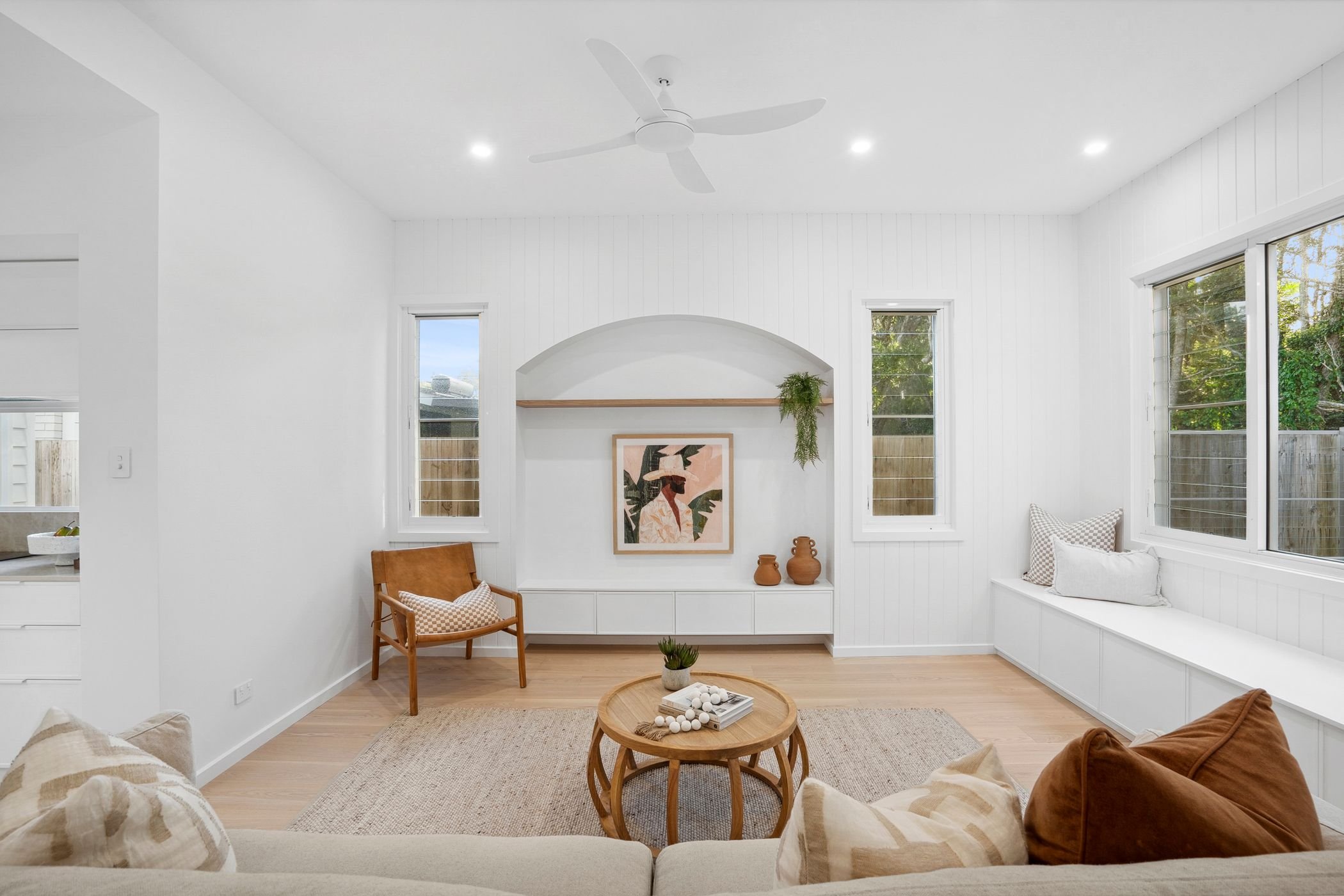 Boutique duplex project in Port Macquarie features modern living room with large windows, and custom built-in TV alcove and window seat with storage.