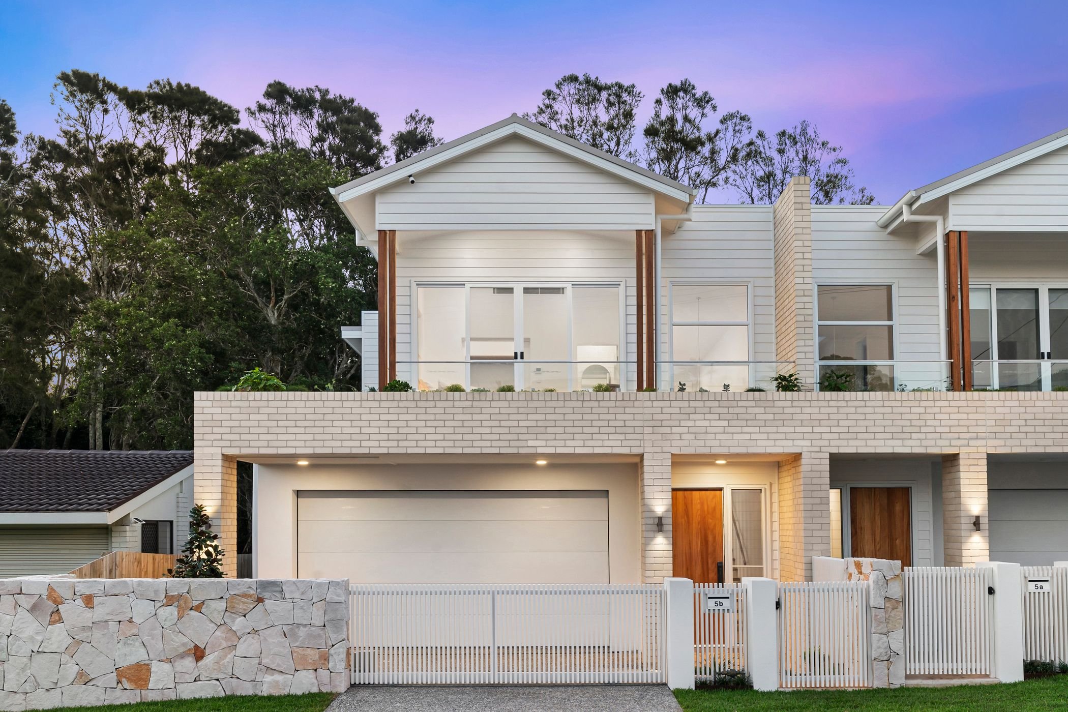 Boutique duplex project in Port Macquarie features brick and weatherboard facade with timber accents, large windows, double garage, stone wall with electric gate.