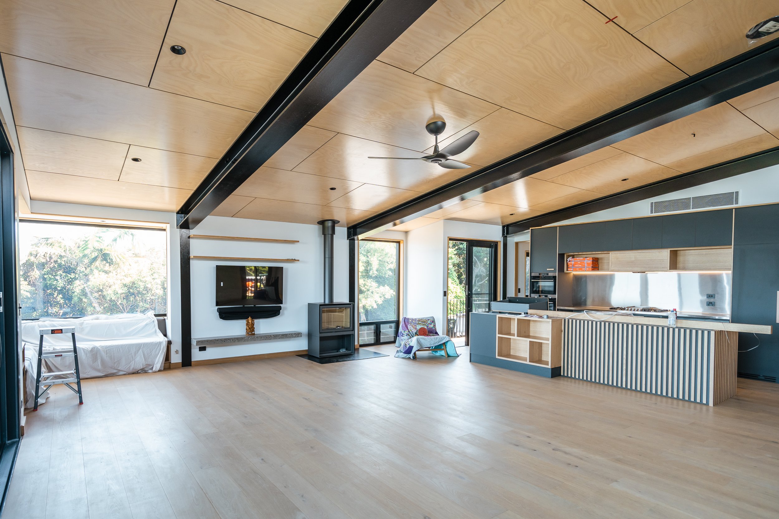 Open-concept living room and kitchen with wooden ceiling, large windows, light wood flooring, and modern furniture.