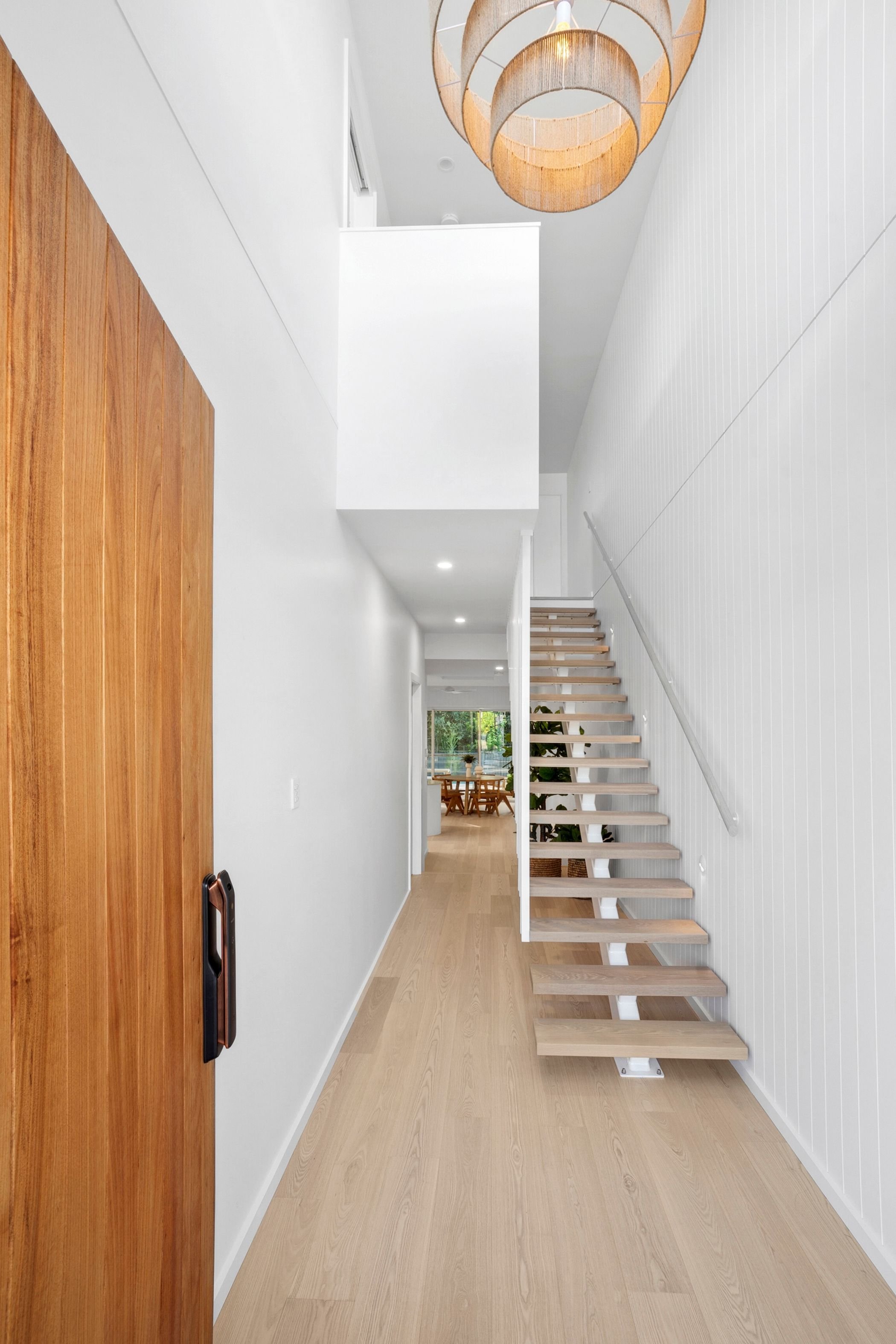 Custom built duplex project in Port Macquarie features modern entryway with timber floors, floating stairs and chandelier.