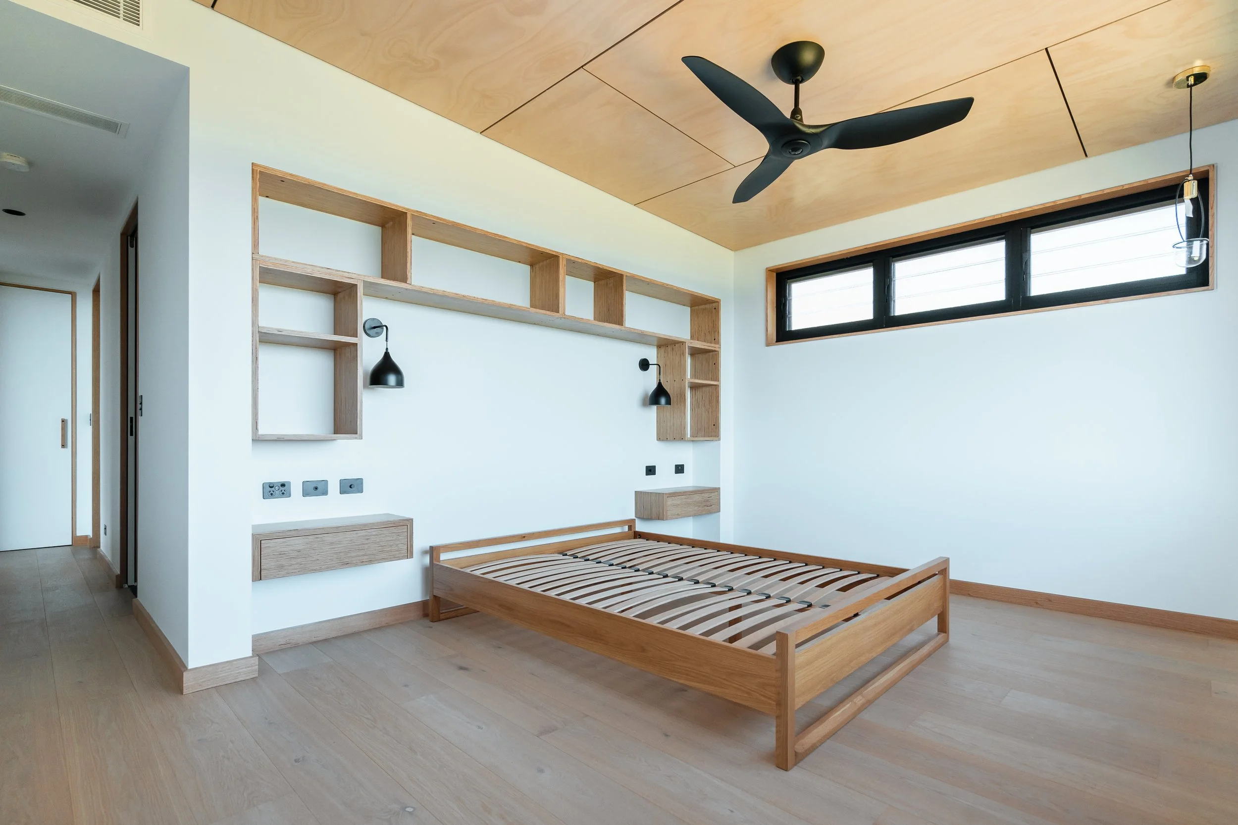 Bedroom in luxury residential building project in Port Macquarie including wall-mounted lamps, custom built-in joinery, a ceiling fan and high windows.