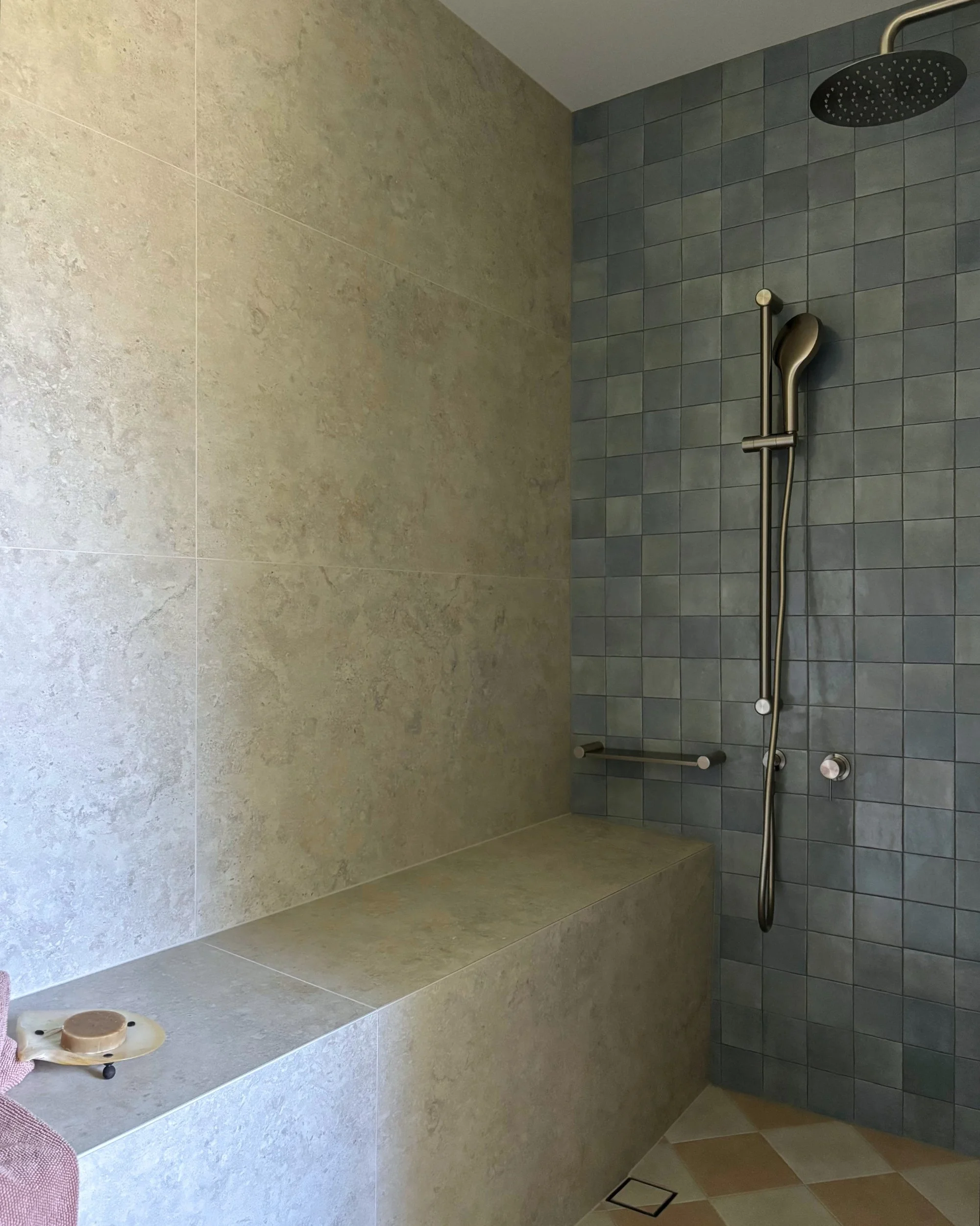 Walk-in shower with heated tiled bench, blue wall tiles and brushed metal shower fittings