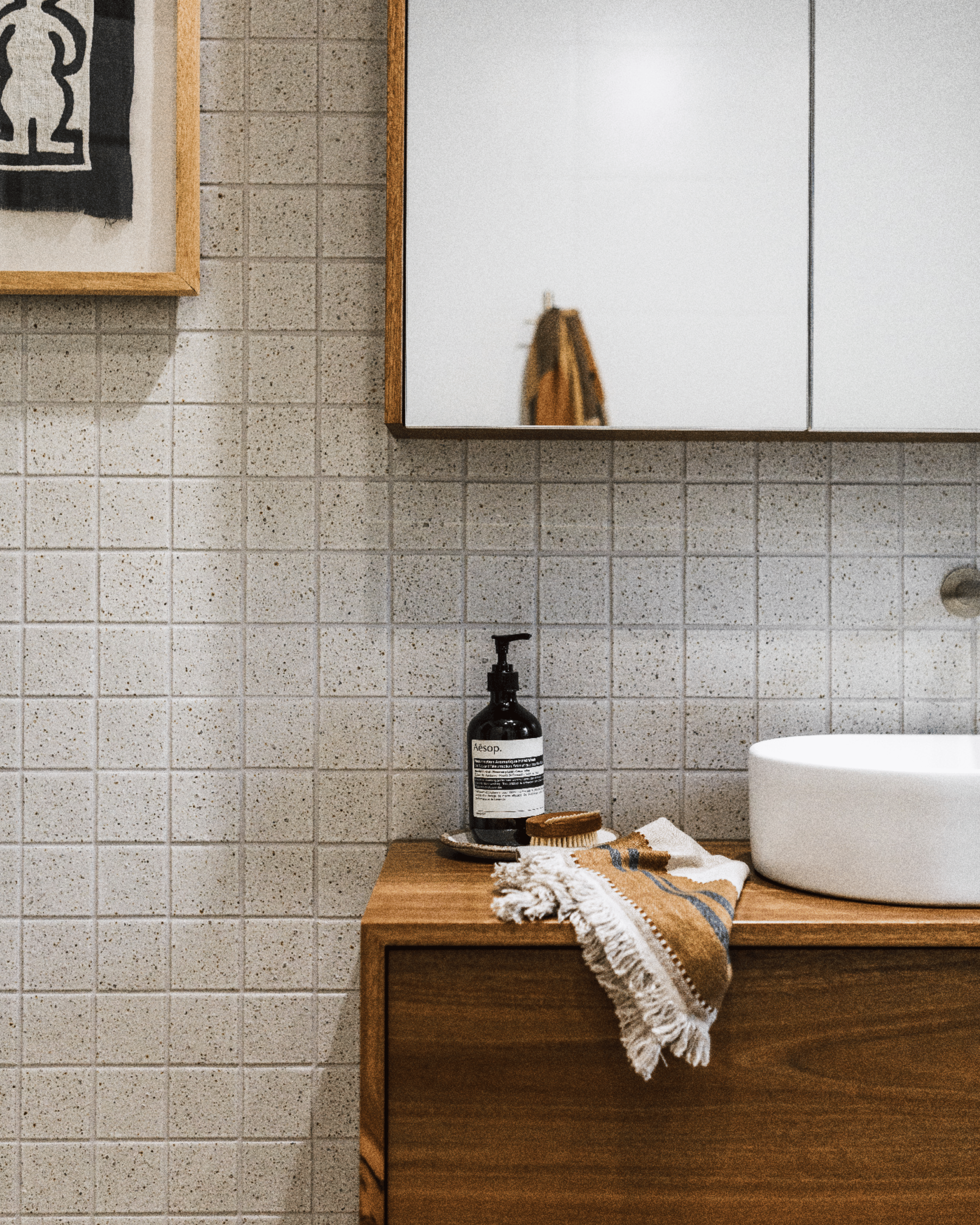 Custom timber vanity with vessel basin, mirrored cabinet and textured wall tiles.