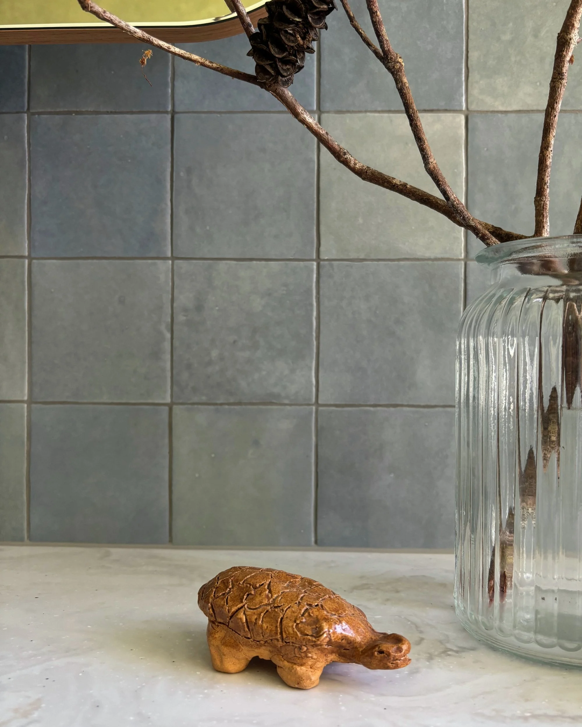 Handmade ceramic turtle displayed on the bathroom vanity against blue tiles
