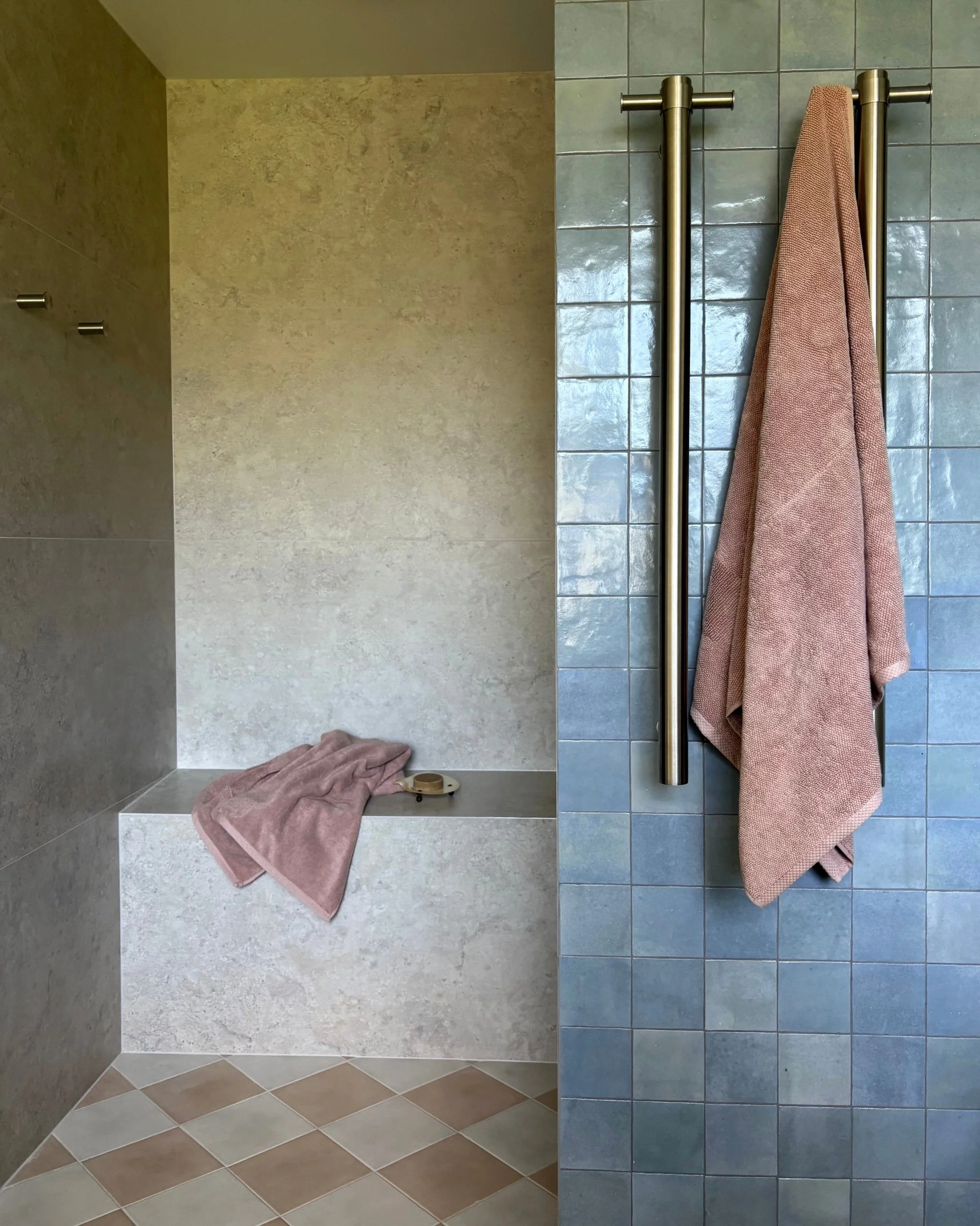 Bathroom detail with tiled shower bench, blue handmade tiles, brushed metal towel rails and soft pink towels
