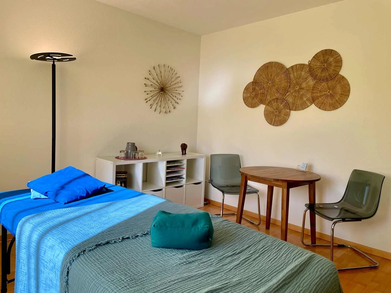Behandlungsraum mit Behanldungsliege für Craniosacral Therapie und einer kleinen Sitzecke für das Gespräch. Der Raum ist hell mit einer Stehlampe in der Ecke.