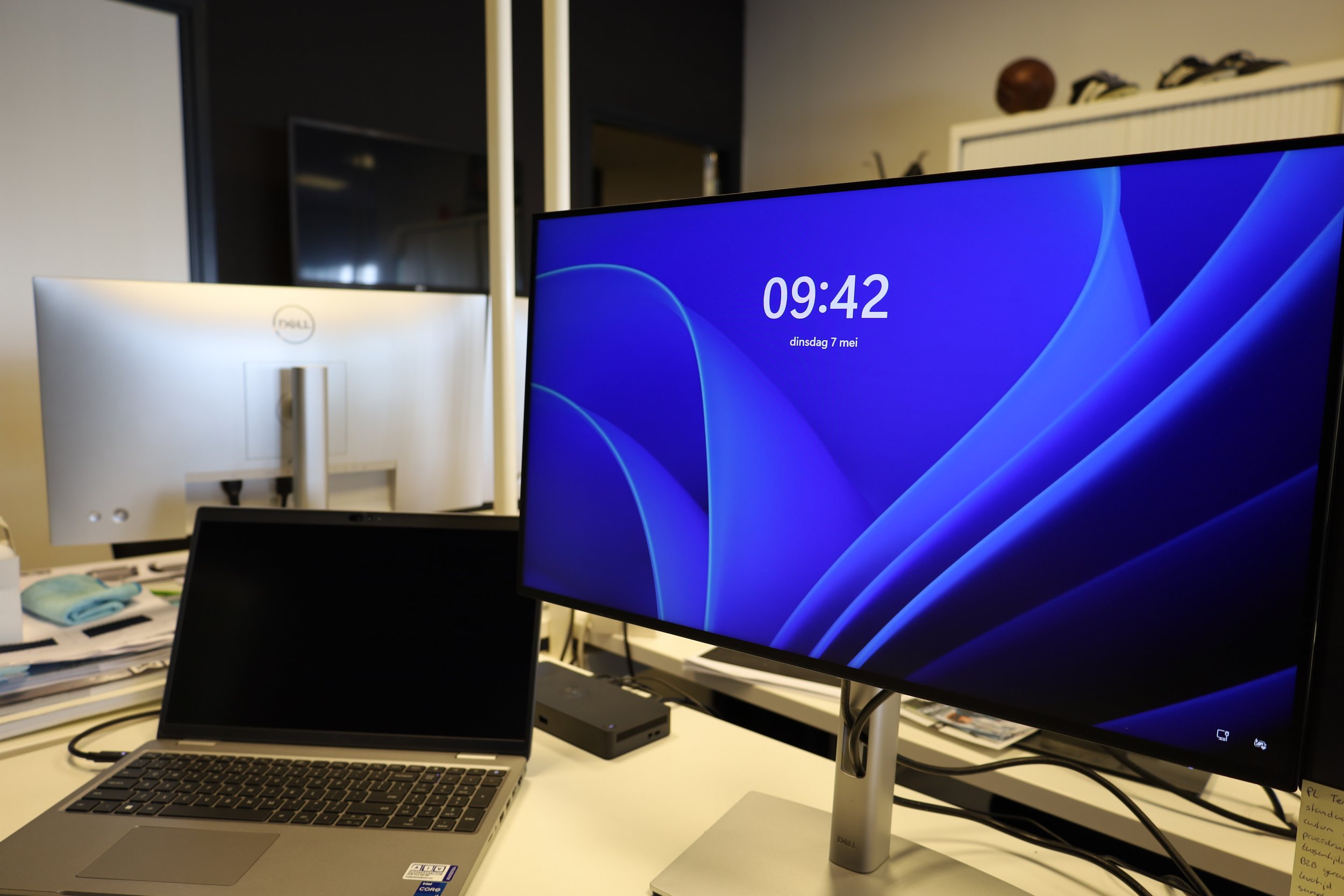 Werkplek met een Dell monitor, een laptop, documenten en een tweede monitor op een kantoor