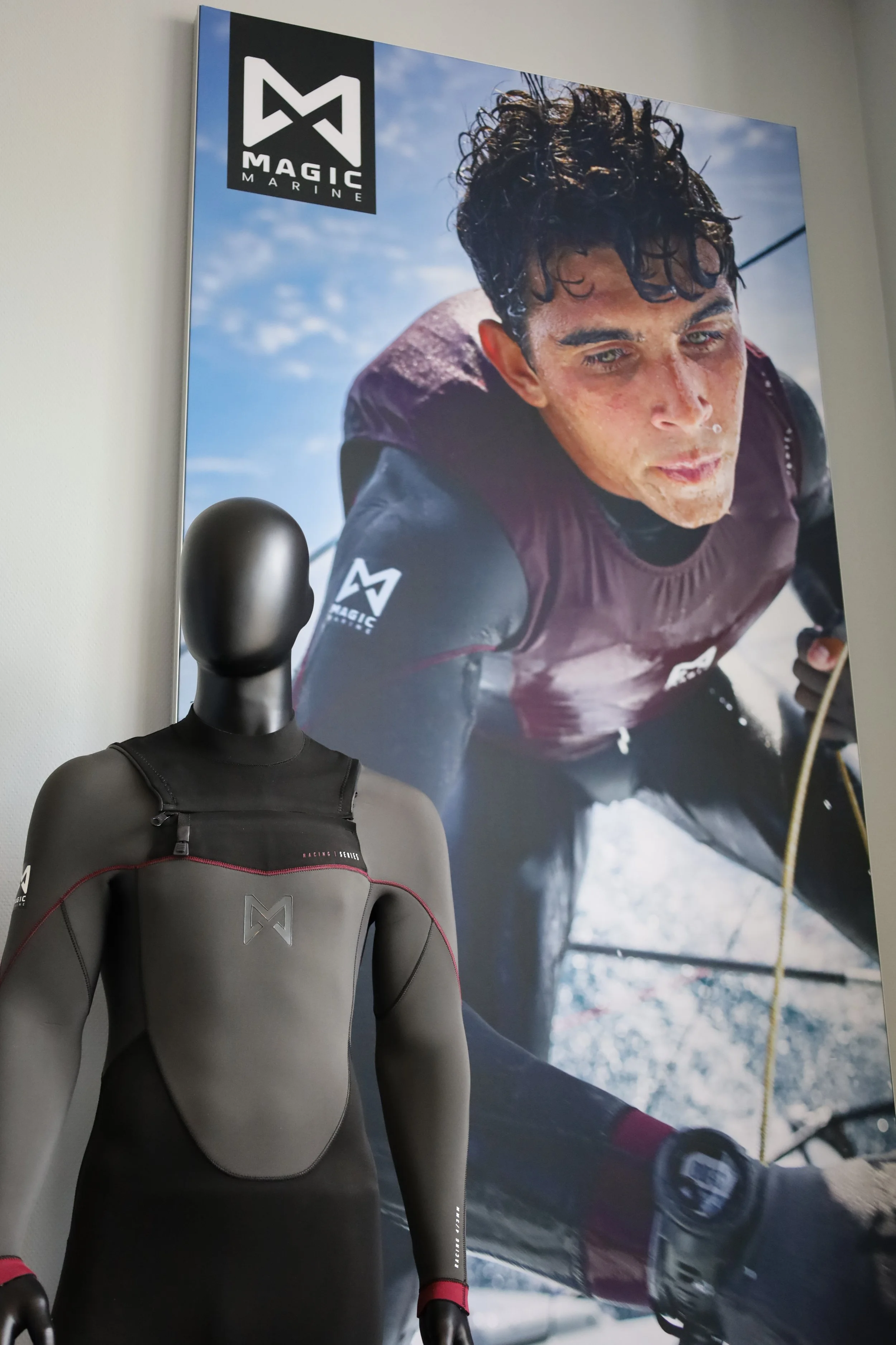 Een mannequin dat Magic Marine kleding draagt, met een grote poster op de achtergrond die een man weergeeft die aan het zeilen is, ook voorzien van het merk Magic Marine.