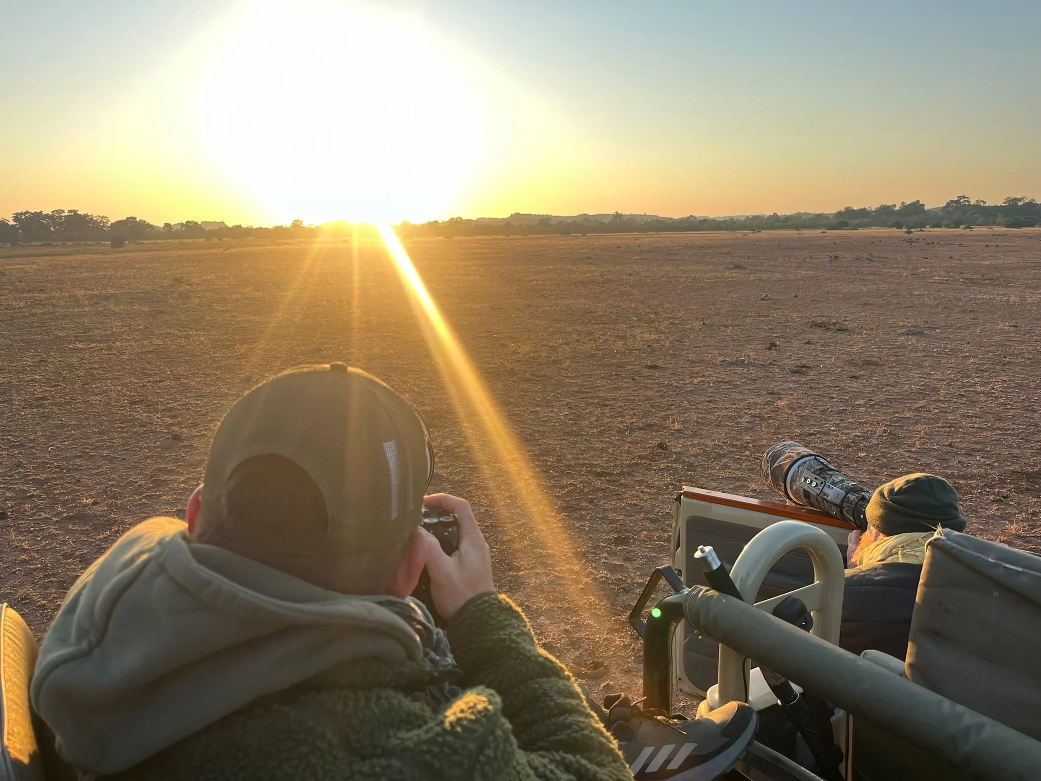 People observing the sunrise over a barren field with telescopes and binoculars, seated in wheelchairs.
