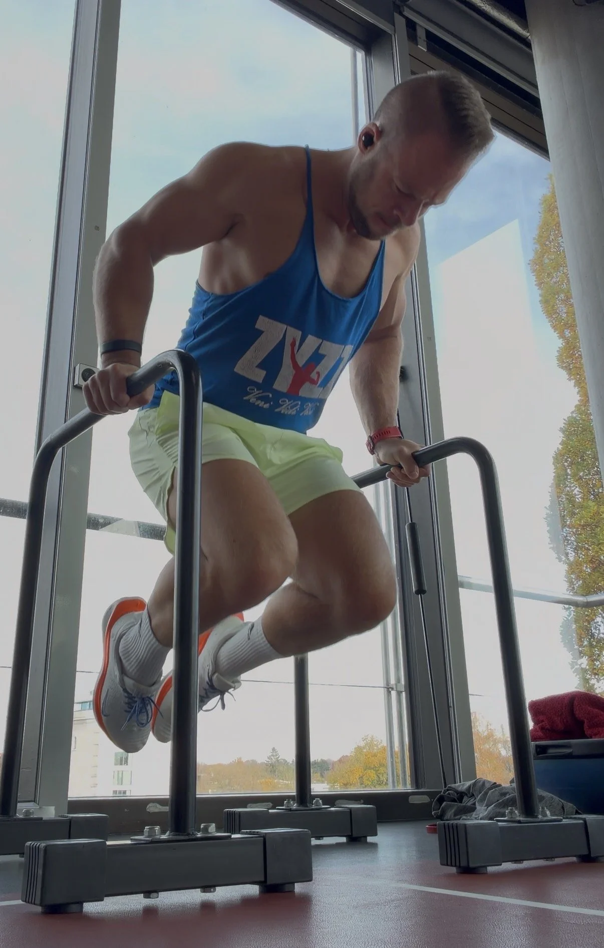Mann trainiert auf einem parallelen Griff. Mann trägt Sportbekleidung, weiße Turnschuhe, Trainer T-Shirt, und Shorts.