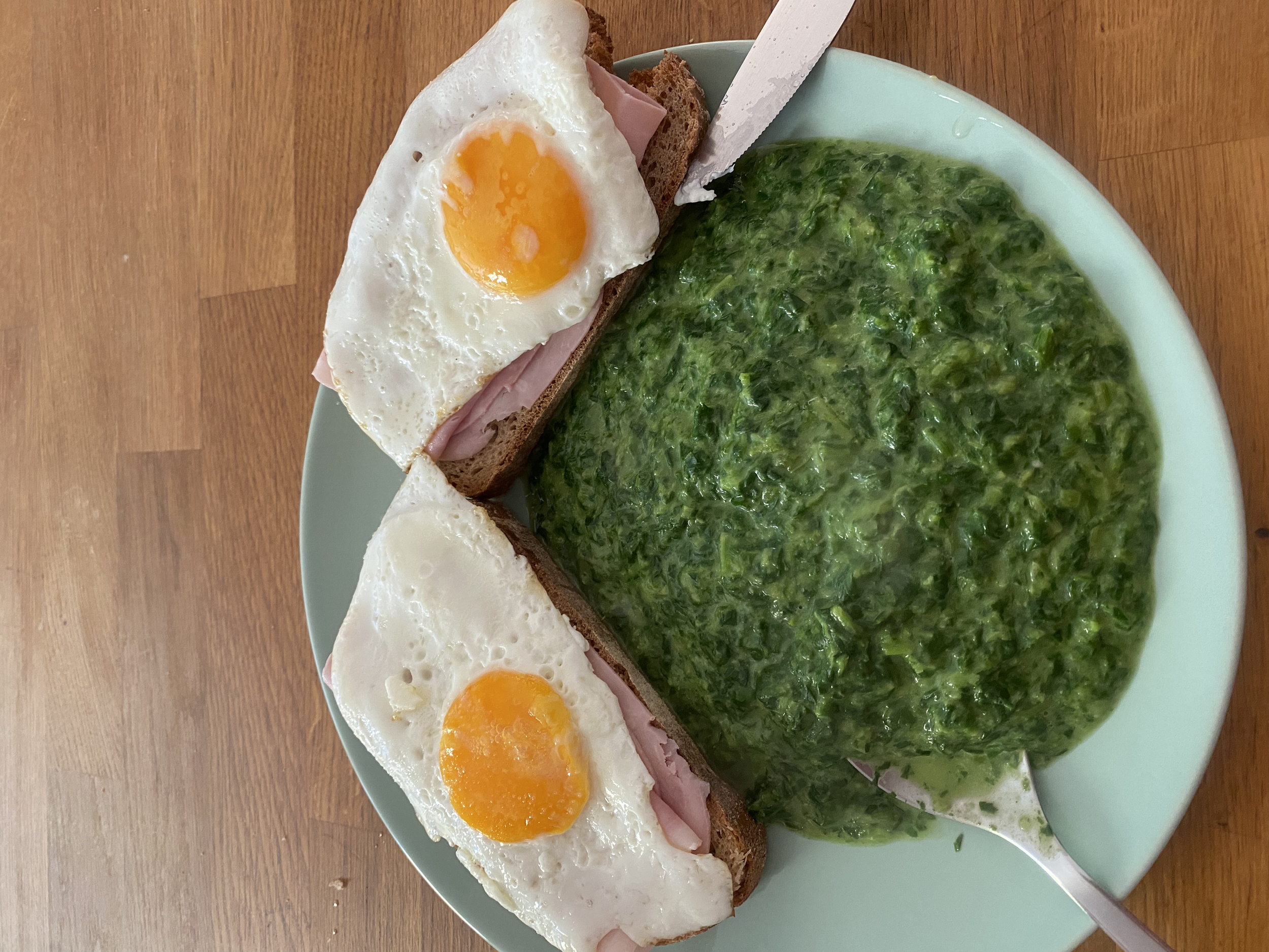 Teller mit zwei Scheiben Brot mit Schinken und Spiegelei, daneben Spinat.