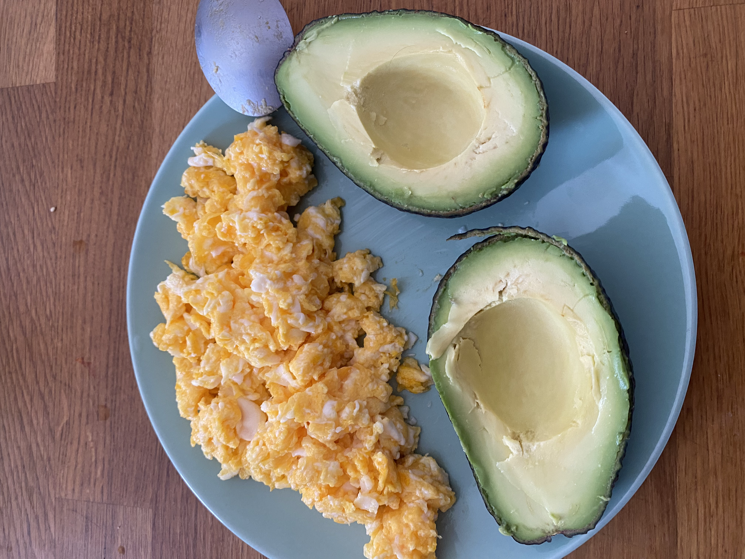 Rührei und Avocado auf einem blauen Teller, mit einem blauen Ei.