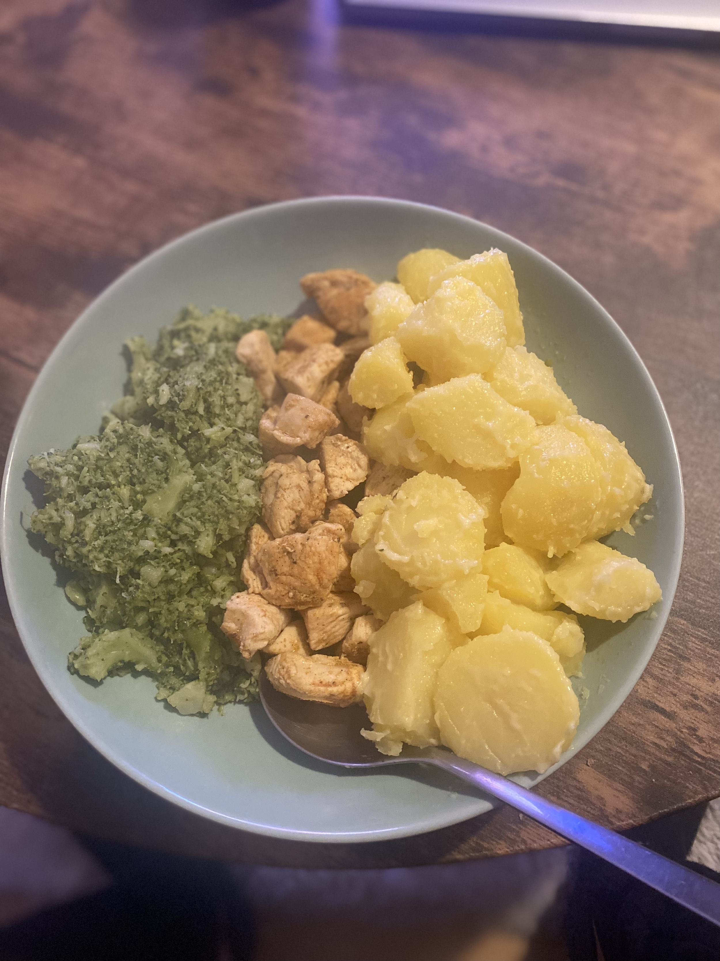Ein Teller mit gekochten Kartoffeln, gebratenem Hähnchen und gedünstetem Brokkoli, auf einem Holztisch serviert.