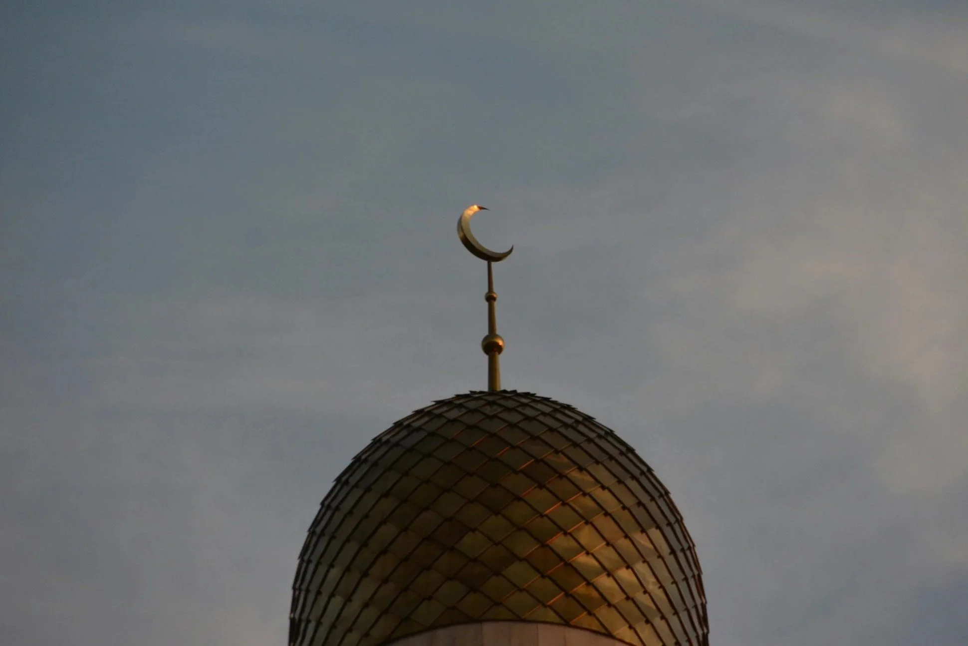 Der goldene Kuppel einer Moschee mit einem Halbmond auf der Spitze gegen den Himmel im Sonnenlicht.