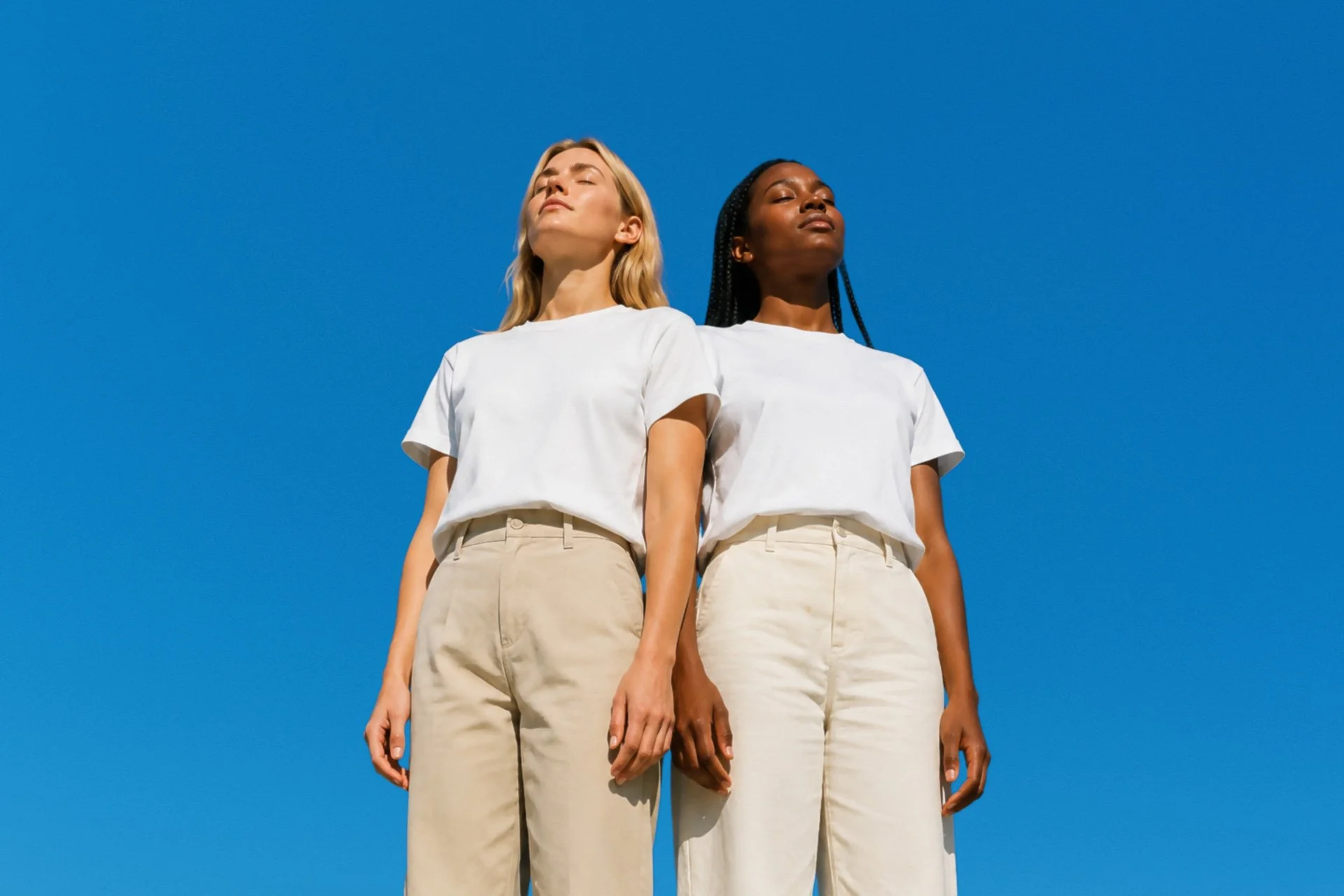 two women facing the sun with closed eyes before a bright blue sky