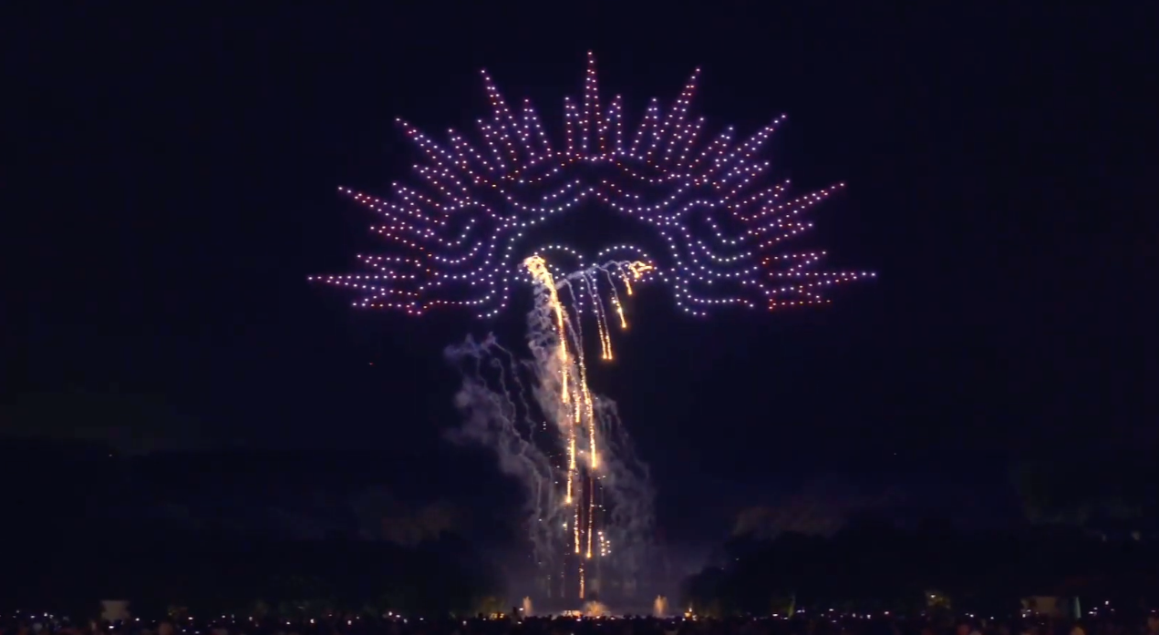 A fireworks display in the night sky resembling a tree or umbrella with purple and gold lights and trails descending from the center.