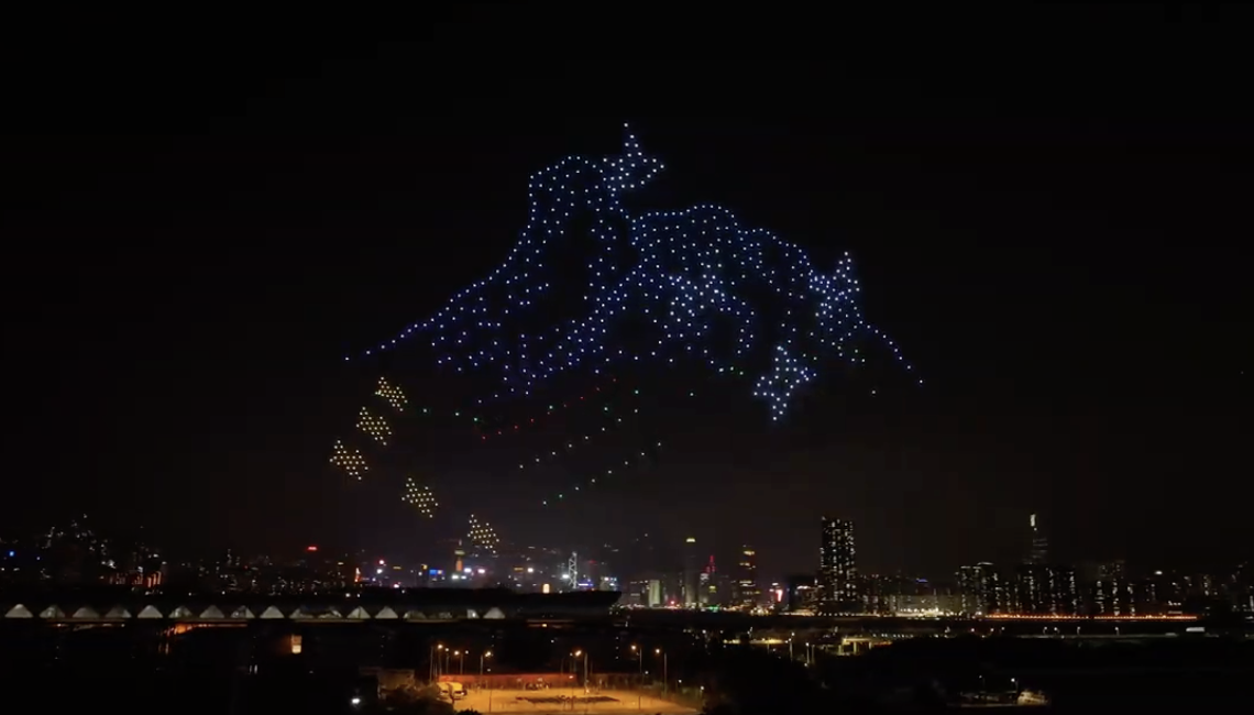 A night sky display of lights forming a dragon above a city skyline with a bridge and illuminated buildings.