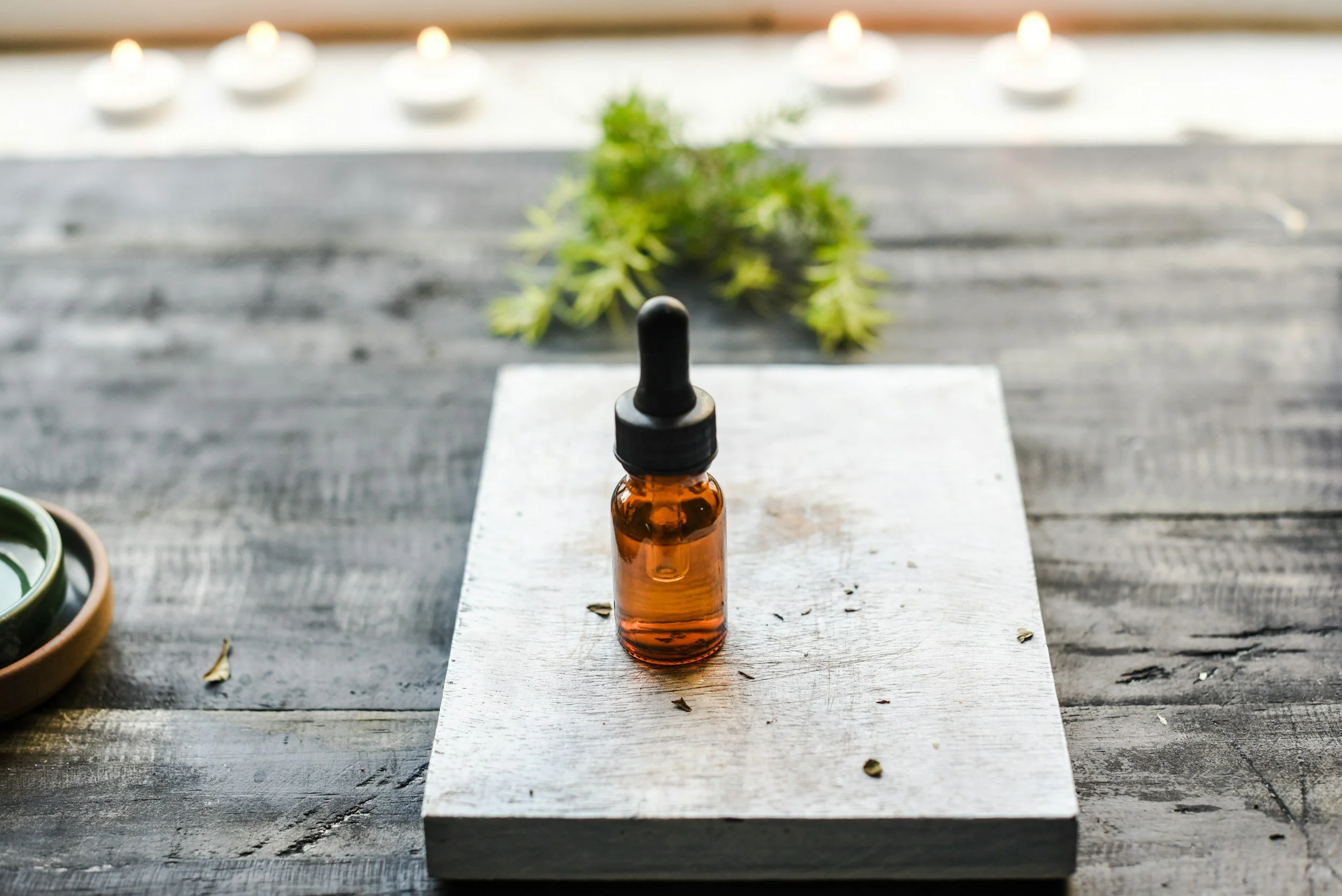 Amber dropper bottle on rustic wooden surface with greenery and candles in background.