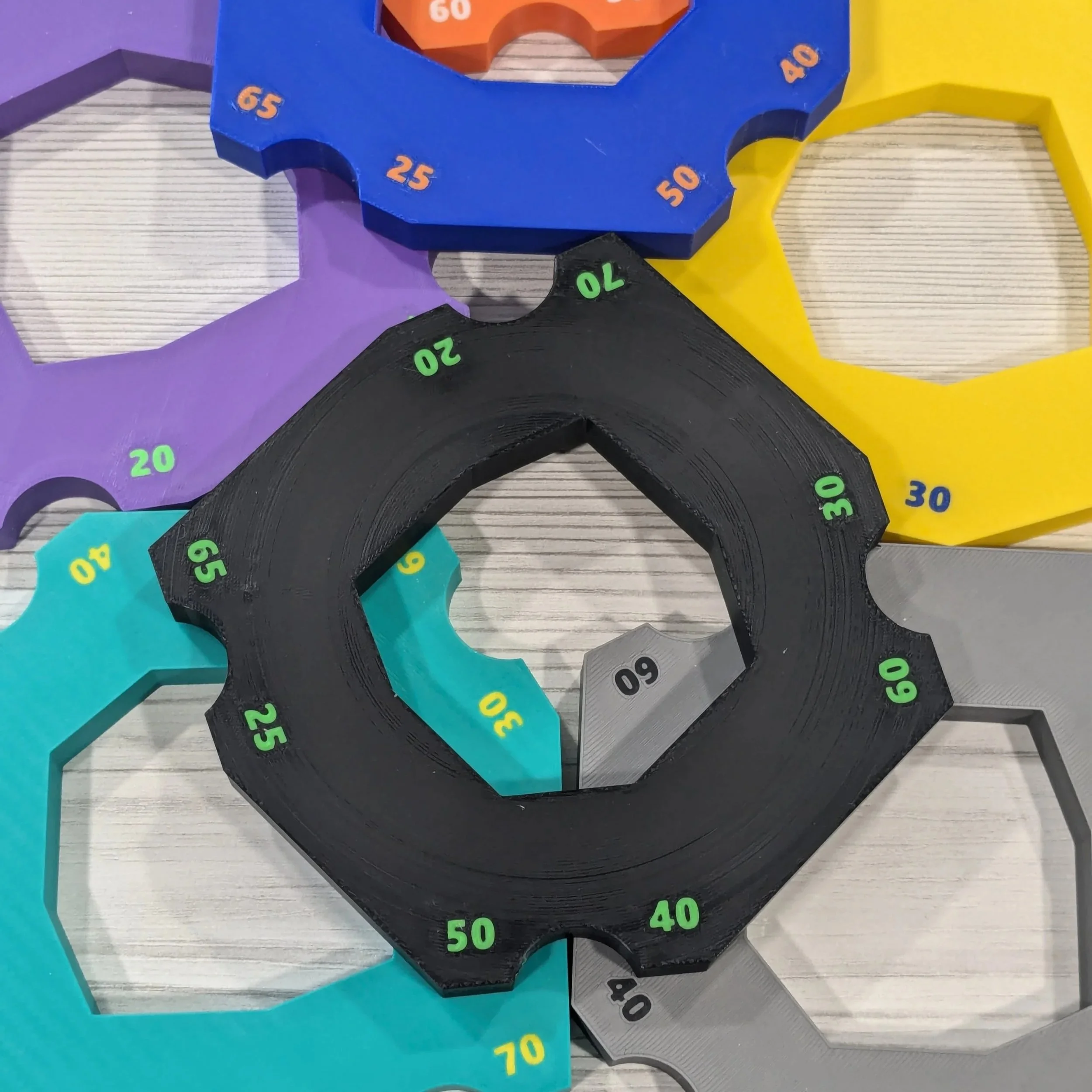 Colorful wooden star-shaped rulers with numbers from 0 to 70 arranged in a circle, placed on a gray wooden surface.