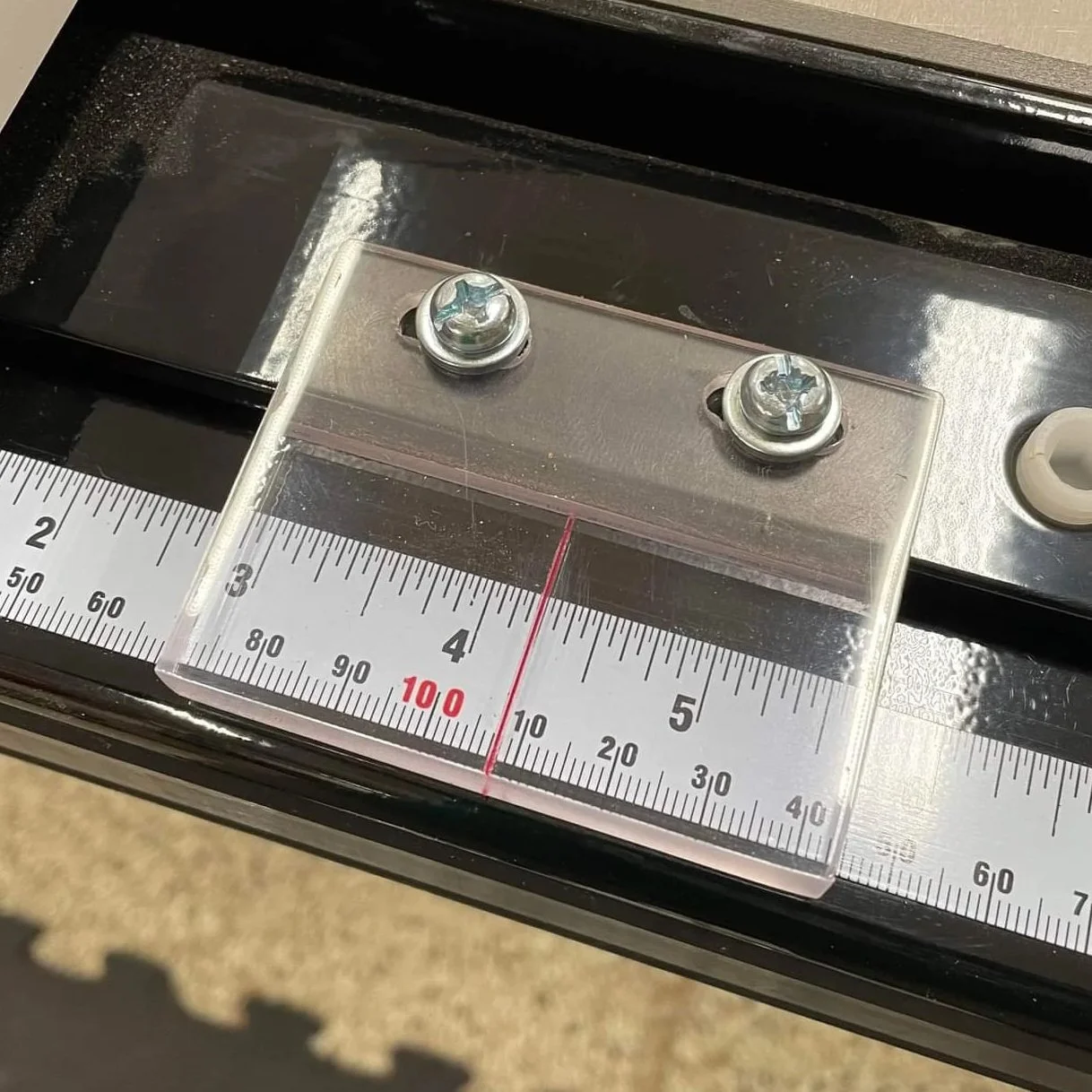 Close-up of a precision ruler with a transparent plastic guide measuring placement of two screws on a metallic surface.