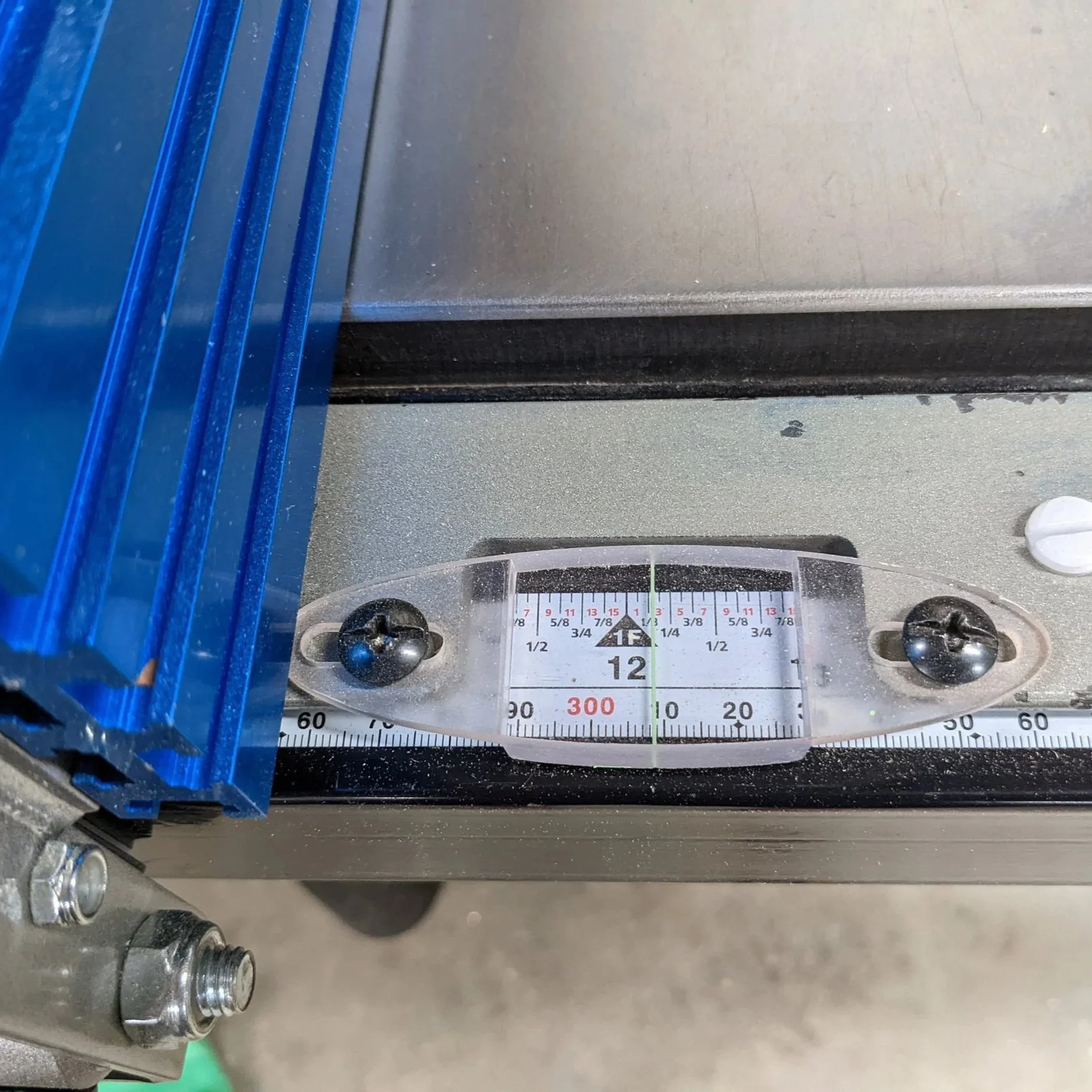 Close-up view of a control panel or gauge with measurement markings, metal screws, and a blue slot on the left side, situated on a gray surface.