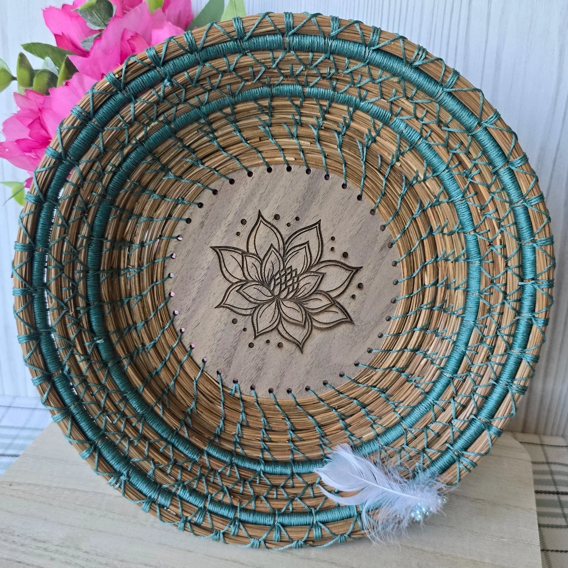 Decorative woven dreamcatcher with a flower and feathers, resting on a wooden surface.