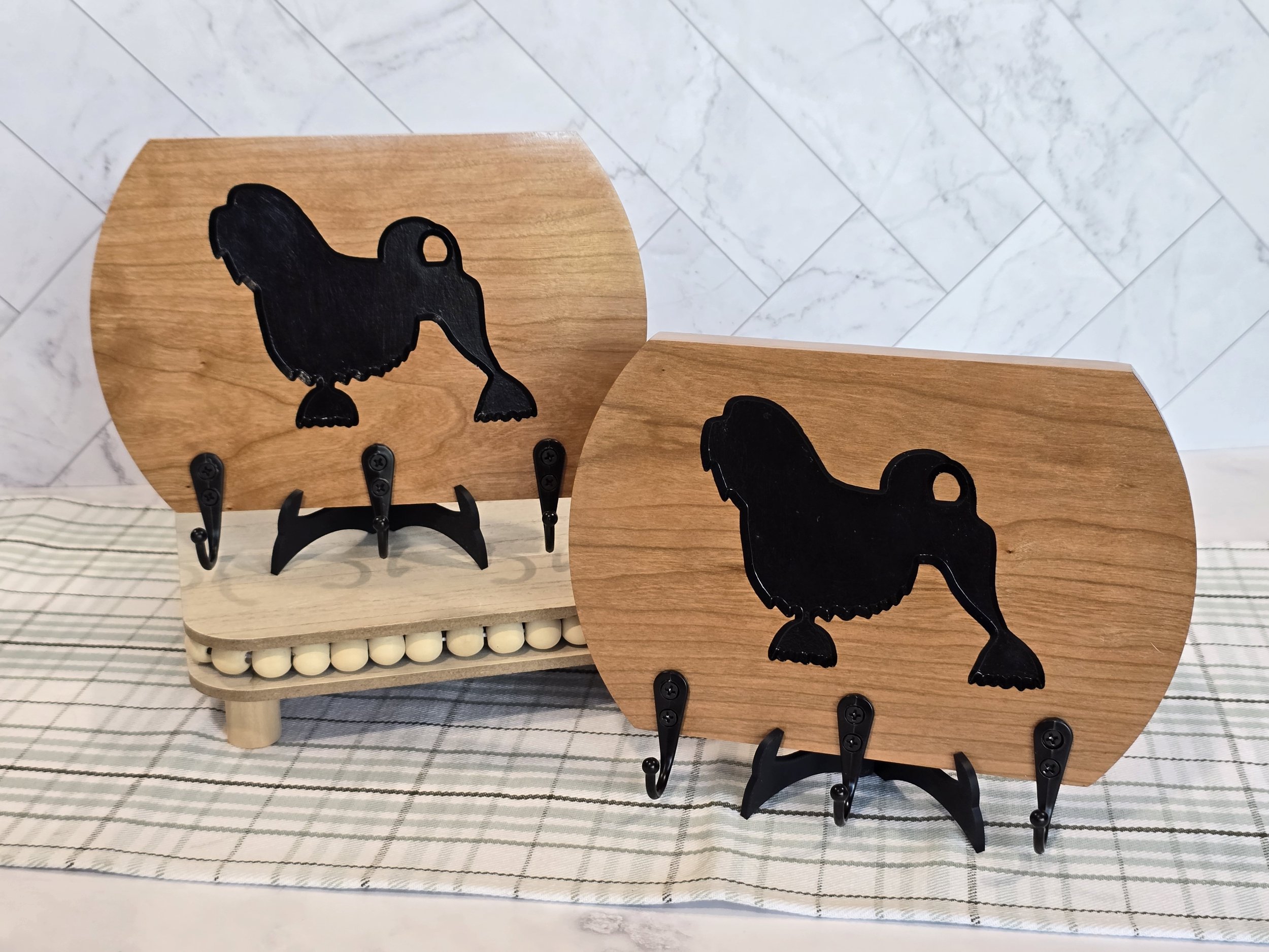Decorative leash holder with Lowchen silhouette accents, placed on a checkered fabric surface, with a marble tile background.