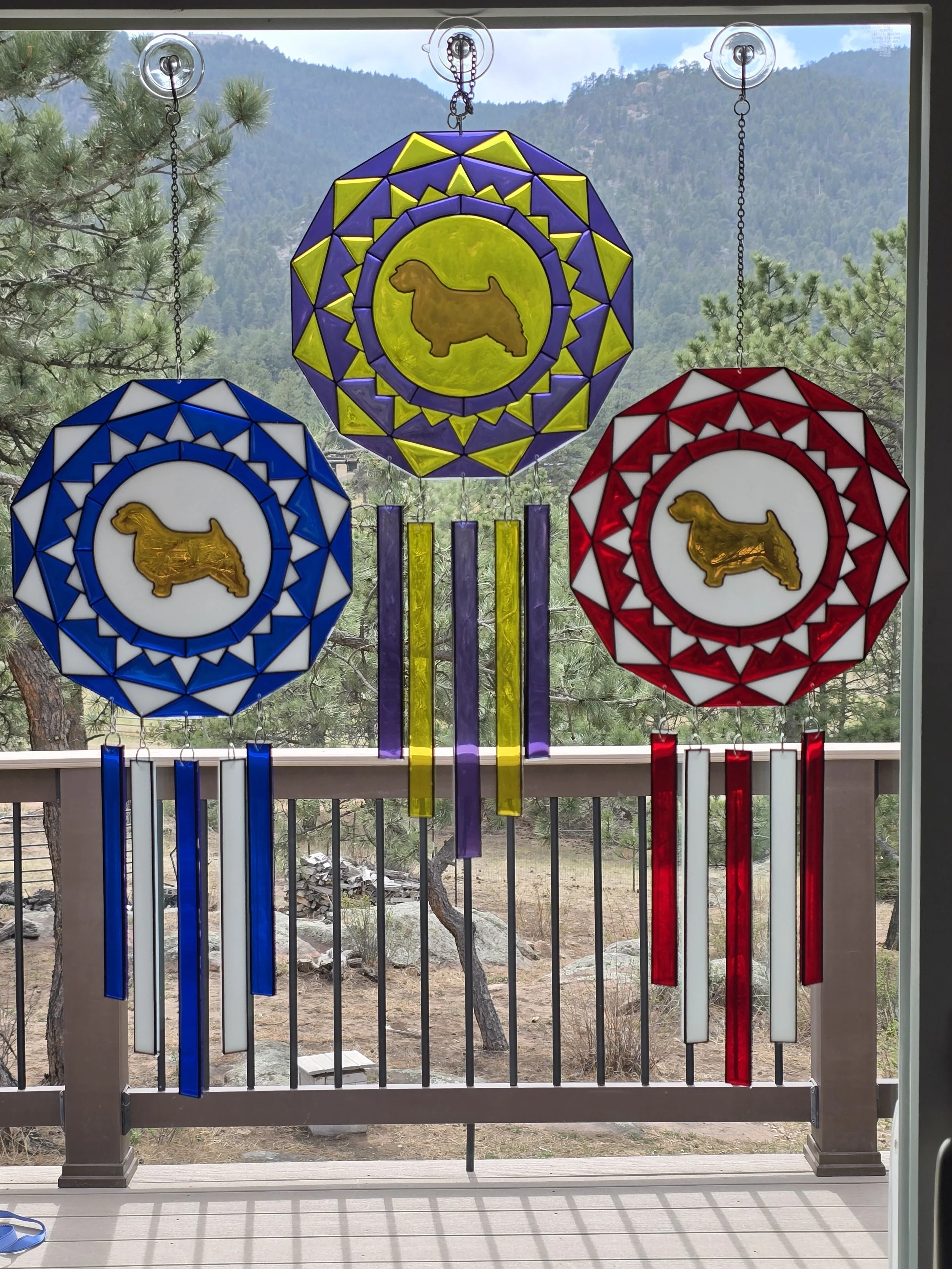 Three resin rosette suncatchers in blue, purple and red with Norfolk Terrier silhouettes and resin ribbons
