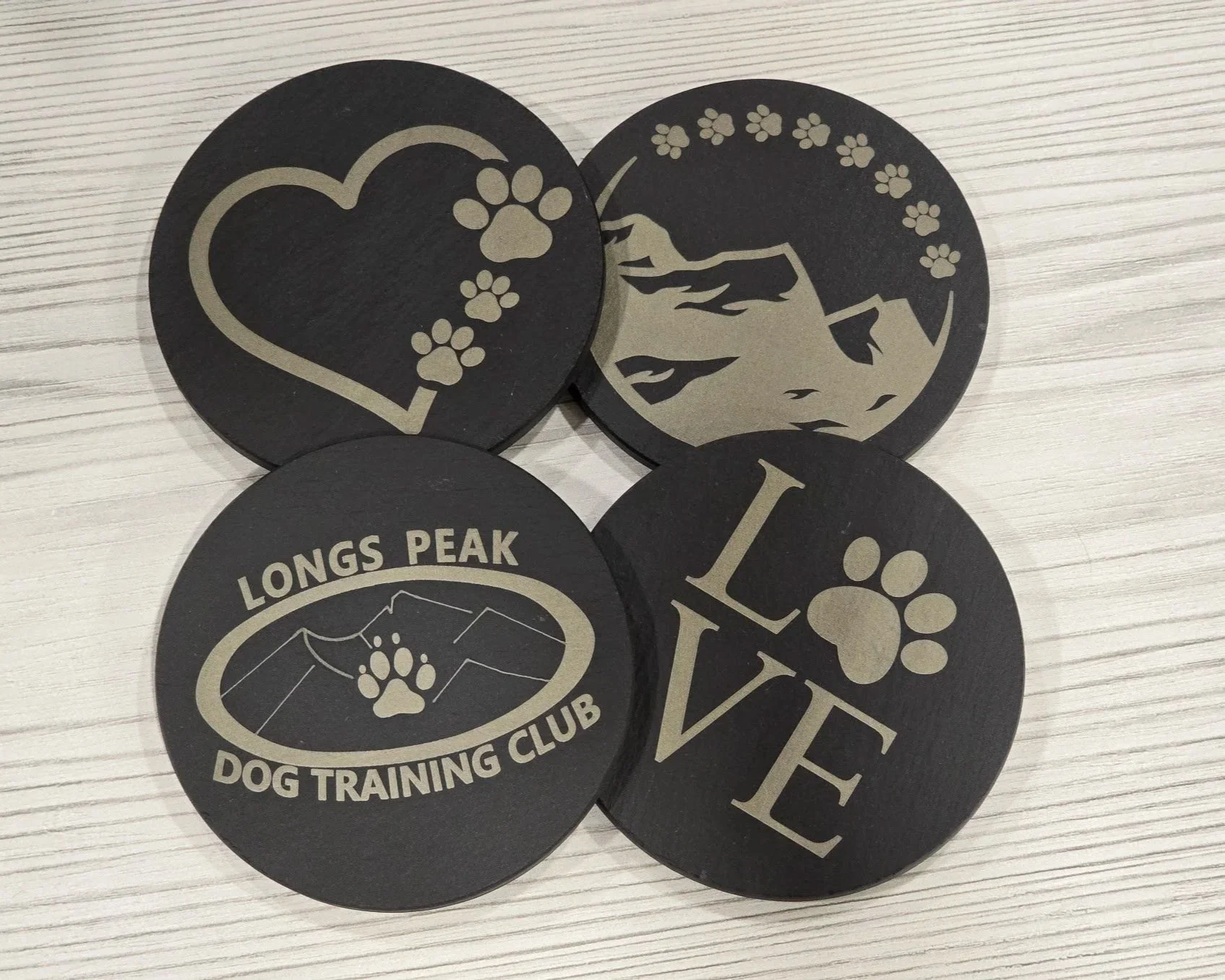 Four round slate coasters with paw print, mountain and Longs Peak Dog Training Club designs