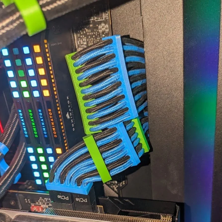 Close-up of a computer motherboard with a cooling system, RGB RAM modules, and cables organized with blue and green cable combs.