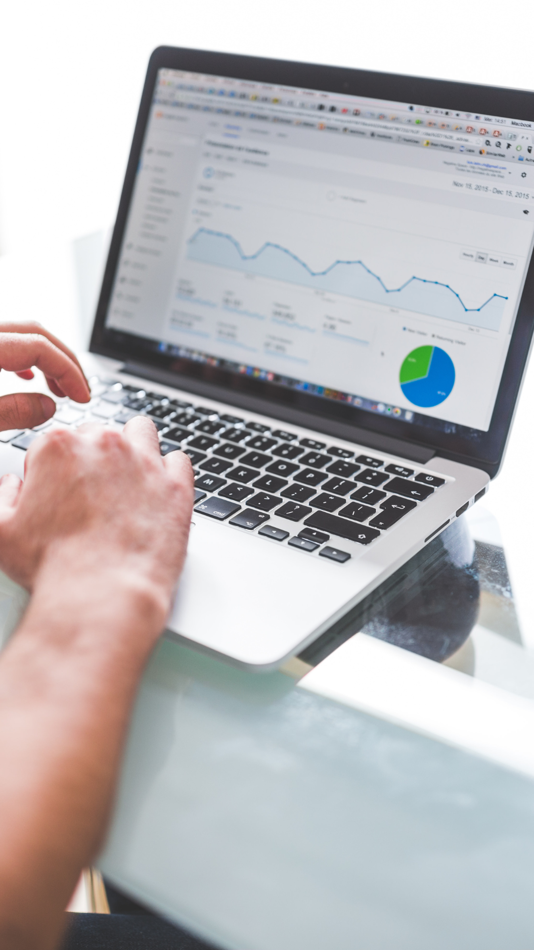 A person working on a laptop computer displaying a analytics or financial dashboard with line graphs and pie charts.